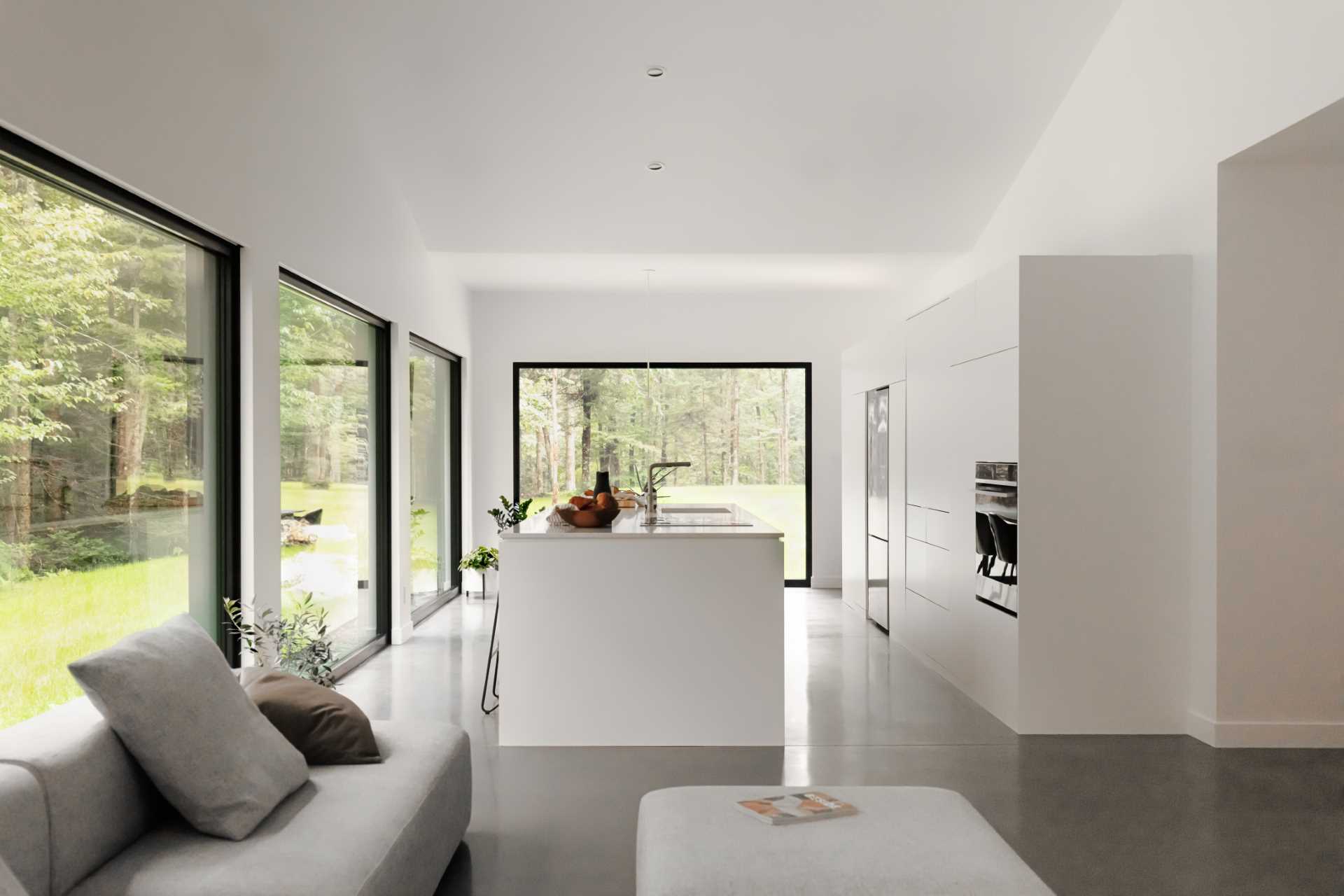 A modern great room with large black-framed picture windows, white walls and cabinets, and a cathedral ceiling.