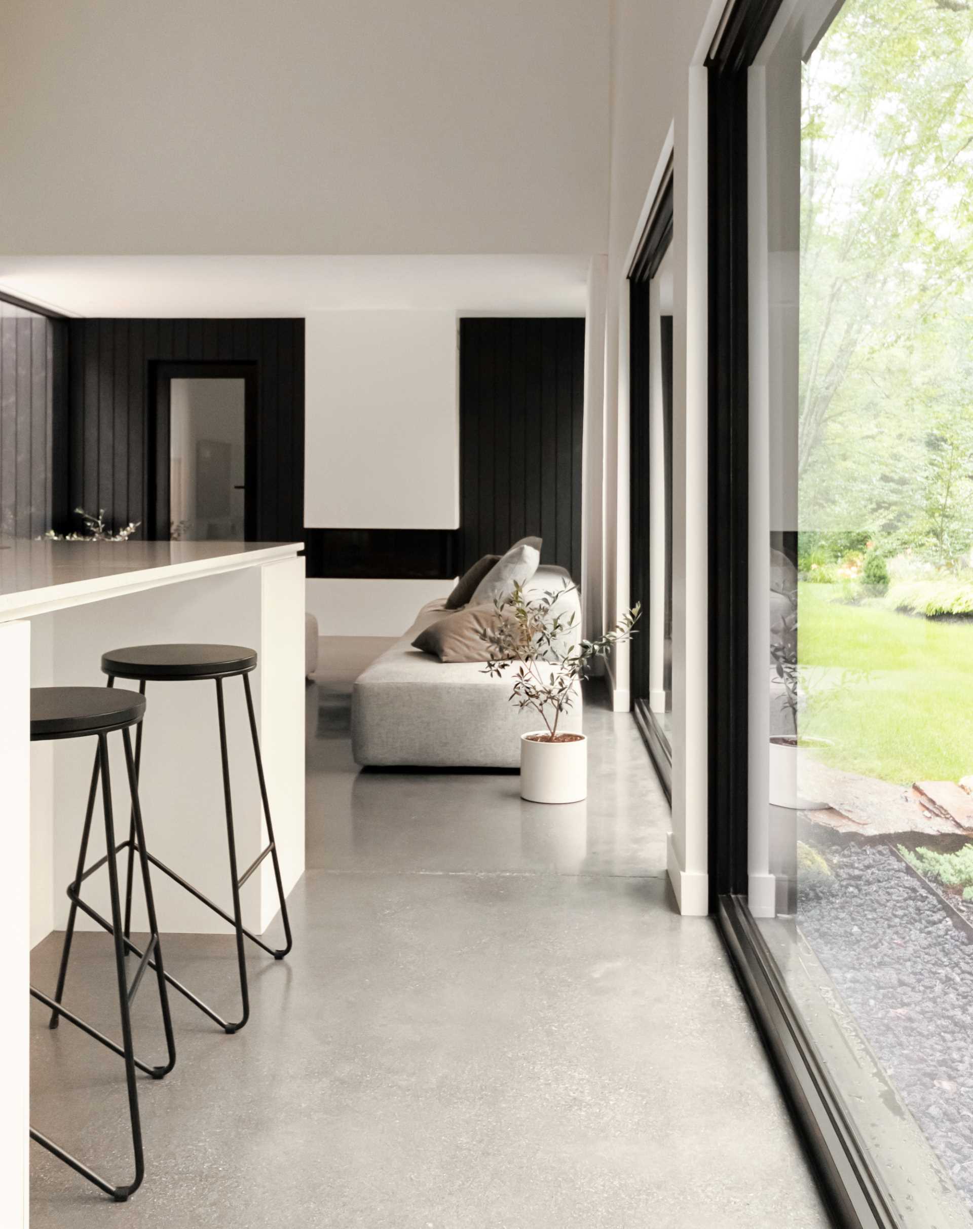 A modern great room with large black-framed picture windows, white walls, and a cathedral ceiling.