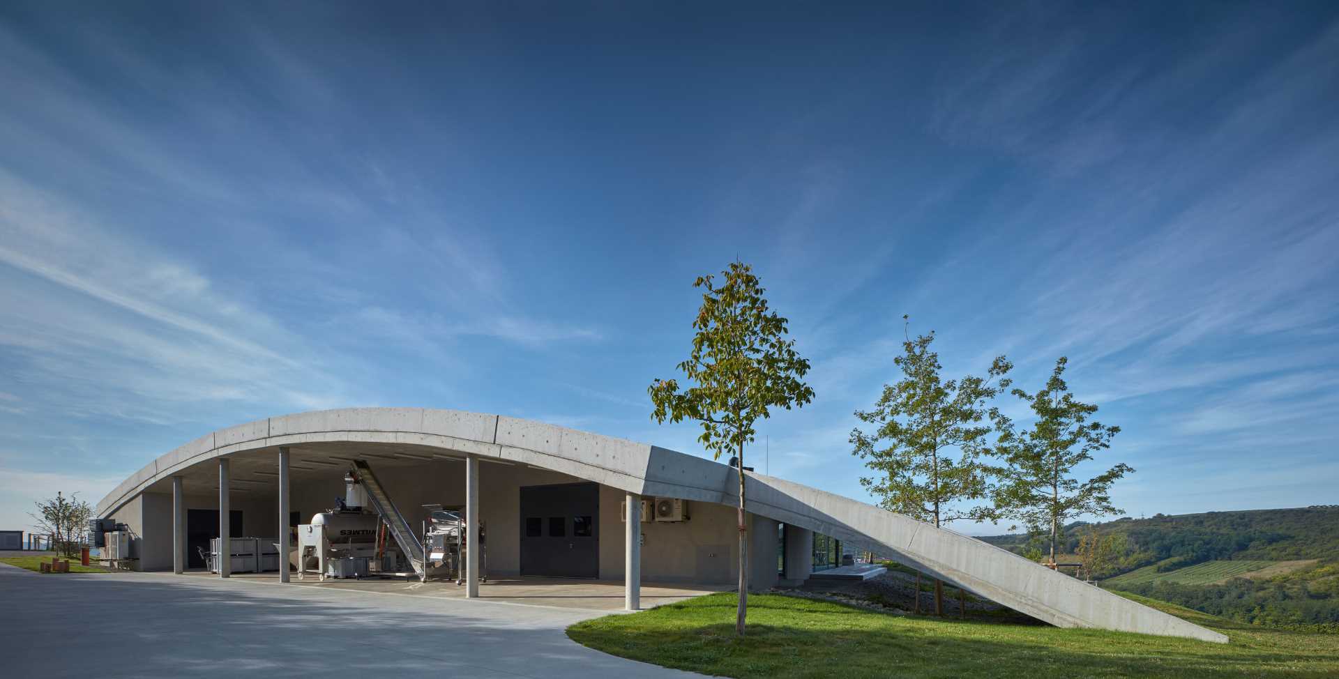 A modern winery that uses exposed concrete, glass, metal, oak, and acacia wood to support the organic form of the building.