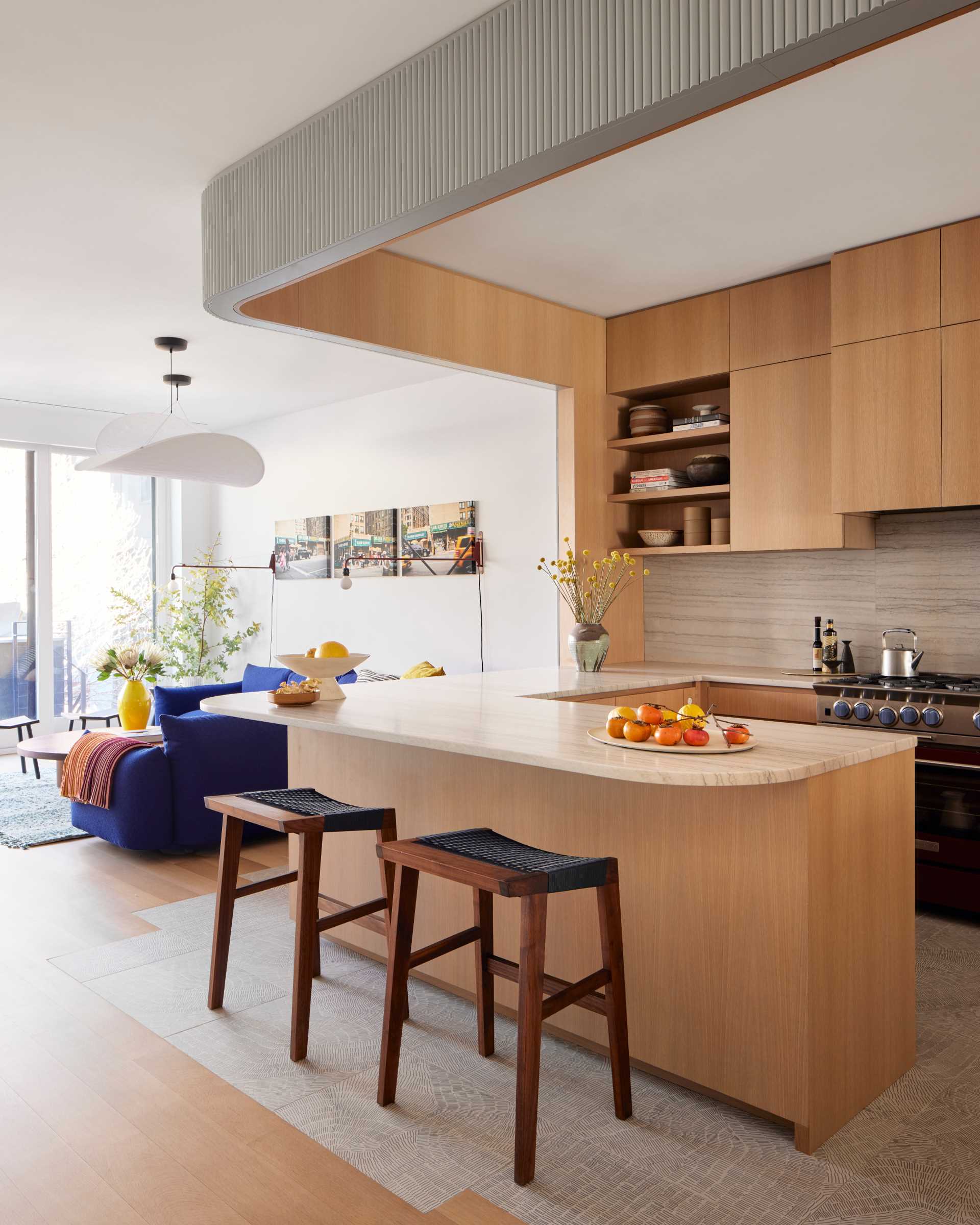 This modern kitchen includes white oak and patterned porcelain tile, and recessed lighting along the dropped arch defines the boundary of the workspace.