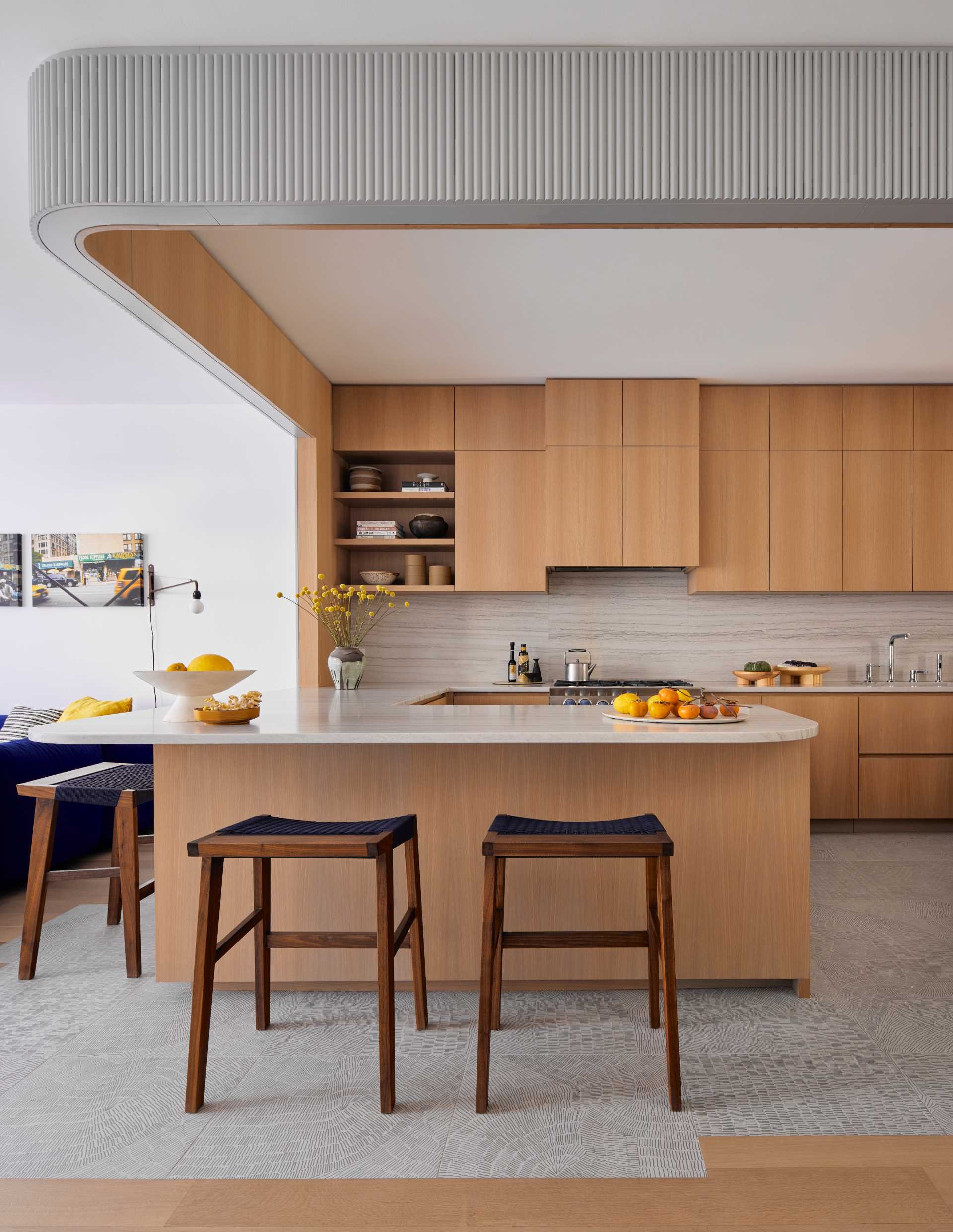 This modern kitchen includes white oak and patterned porcelain tile, and recessed lighting along the dropped arch defines the boundary of the workspace.