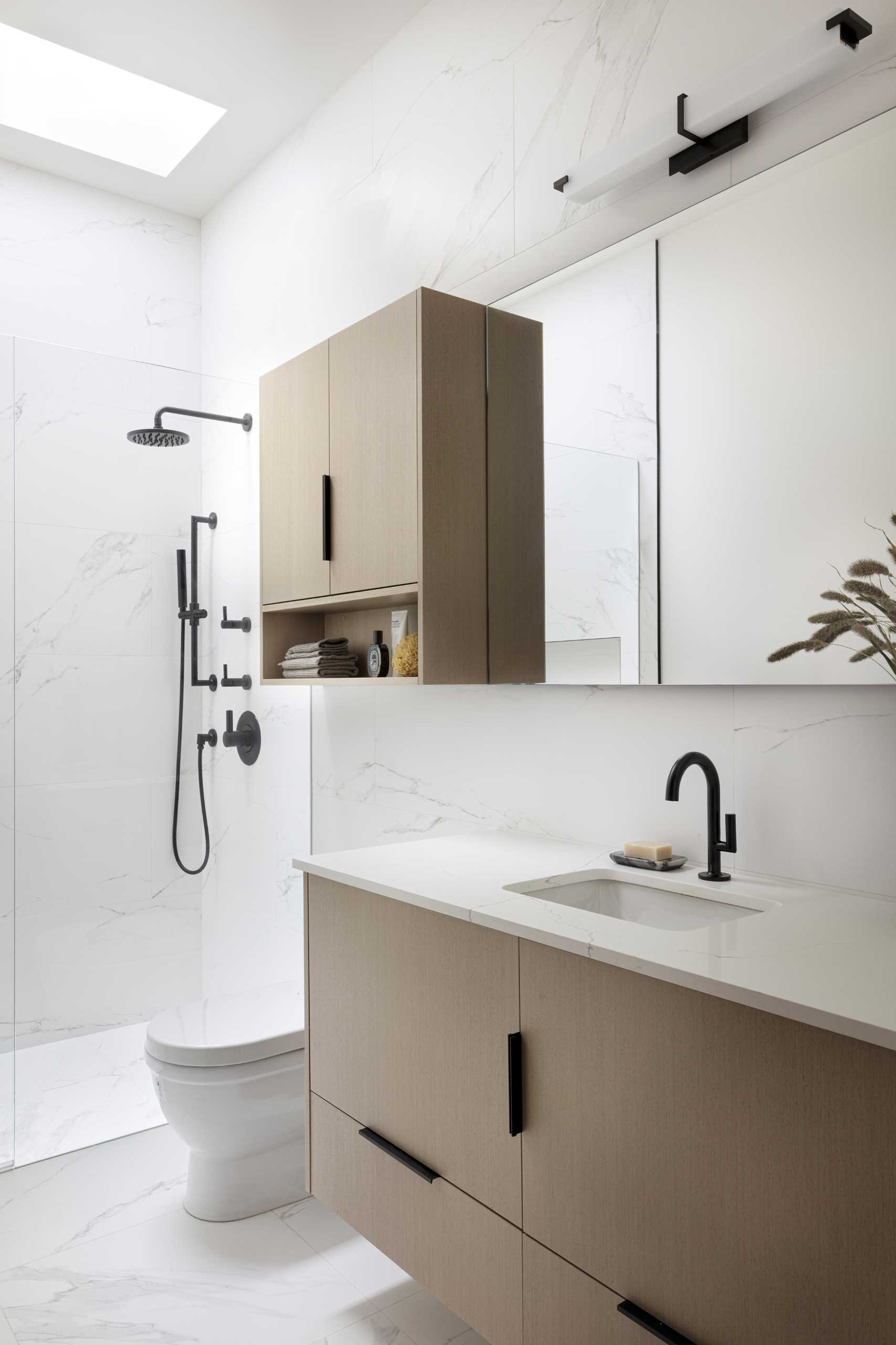 A modern bathroom with light walls and countertop, and a skylight. Black accents provide a contrasting element.