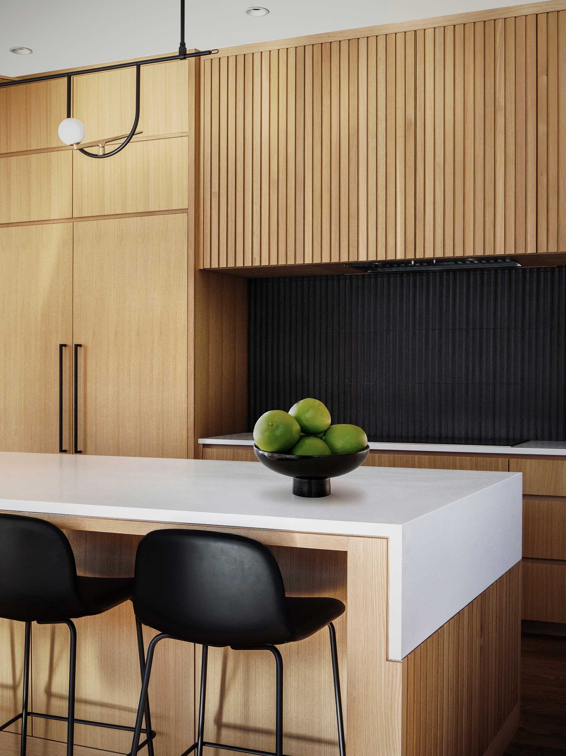 A modern kitchen with an island includes rift-sawn white oak veneer cabinets and concrete-finish quartz countertops. 