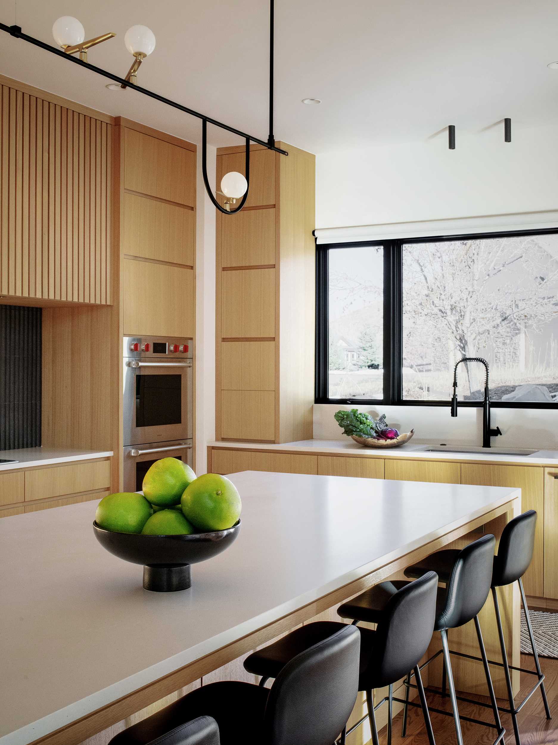 یک آشپزخانه مدرن با یک جزیره شامل کابینت‌های روکش بلوط سفید اره‌شده و میزهای کوارتز با پوشش بتنی است. 