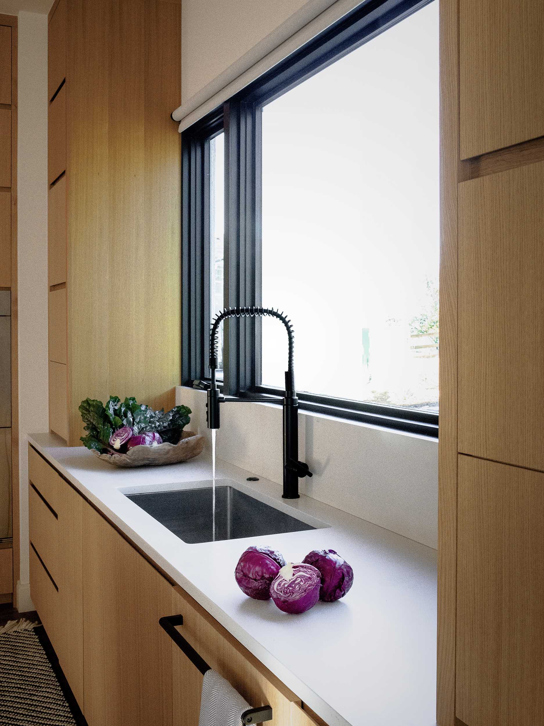 A modern kitchen with an island includes rift-sawn white oak veneer cabinets and concrete-finish quartz countertops. 