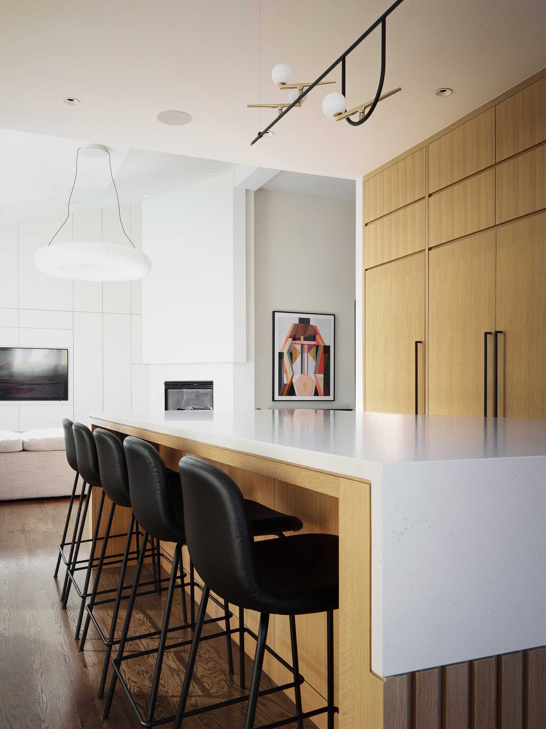یک آشپزخانه مدرن با یک جزیره شامل کابینت‌های روکش بلوط سفید اره‌شده و میزهای کوارتز با پوشش بتنی است. 