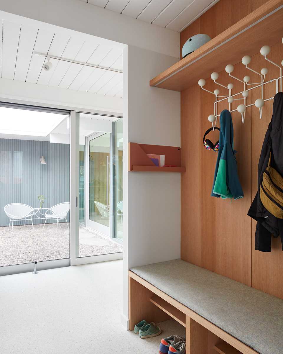 A small mud room by the powder room includes a built-in bench, coat hooks, and a shelf above.