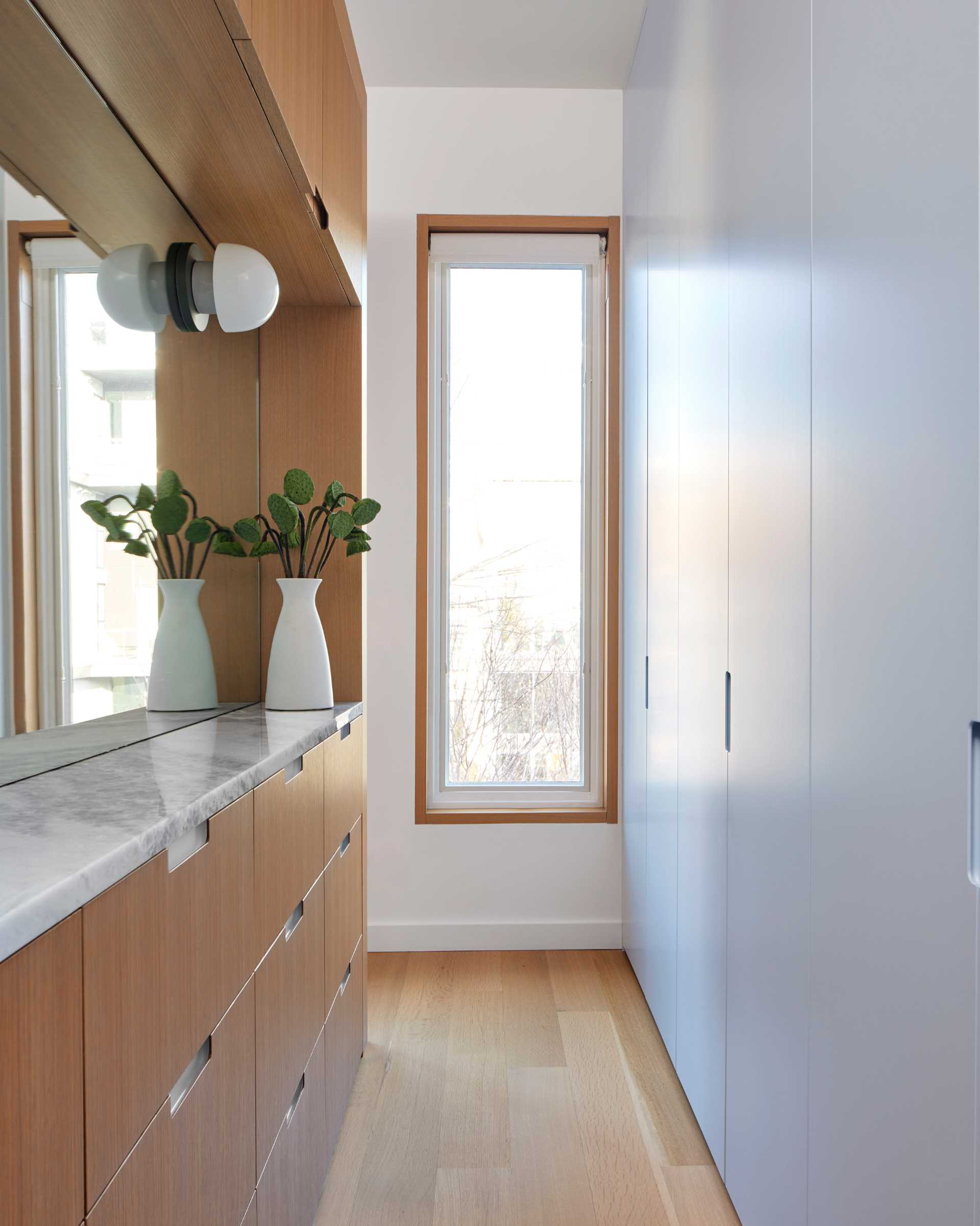 The custom closet wall is painted the same blue-grey as the main floor, while a mirror helps to reflect the light in the narrow space.