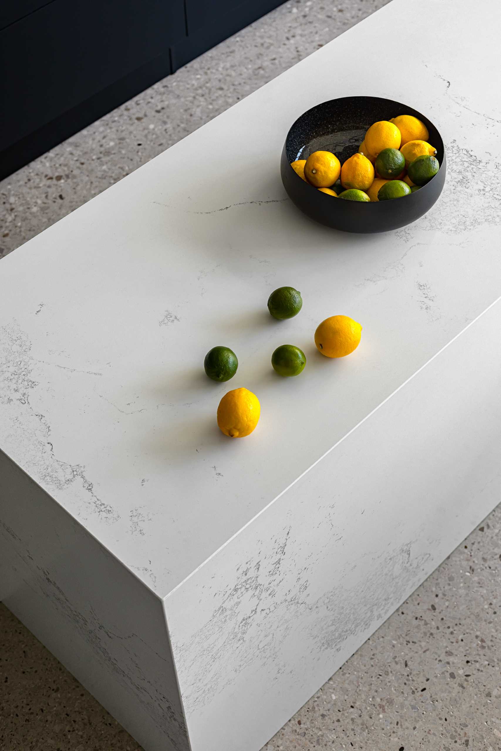 A modern kitchen with a white stone island with subtle veins and minimalist black cabinets.