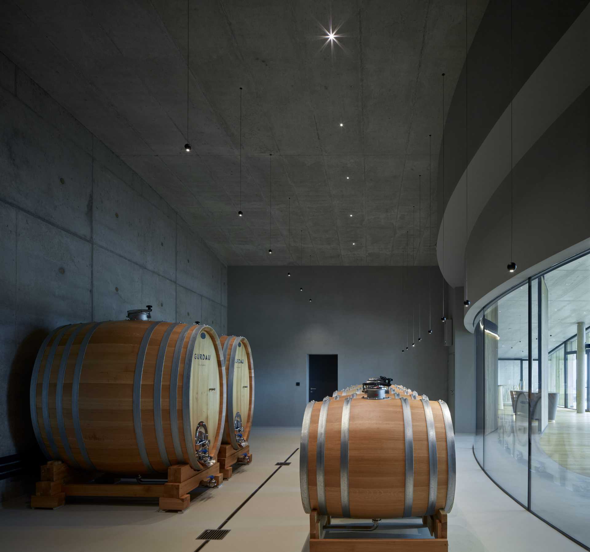 A selection of wine barrels are housed behind a curved glass wall, providing visitors with a glimpse of the wine-making process.