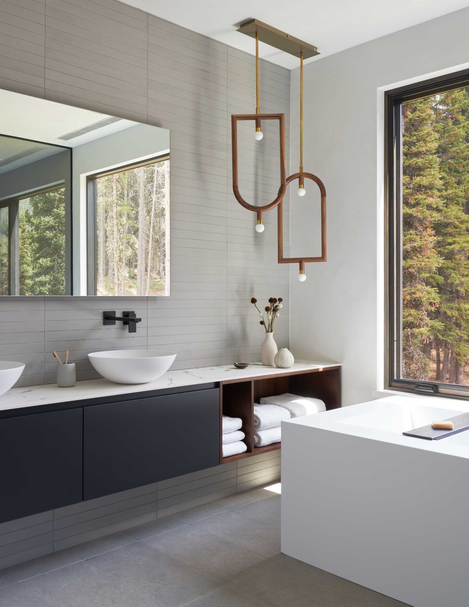 A modern bathroom with long rectangular grey tiles installed in a horizontal layout on the wall, while unique pendant lights fill the corner of the room.