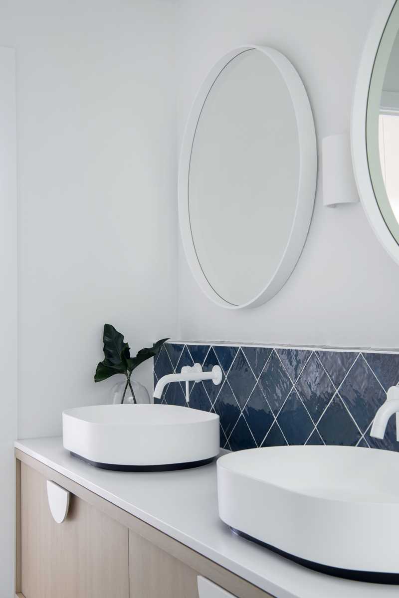 In this bathroom, round mirrors adorn the wall above the vanity, while blue tiles add a subtle but colorful accent.