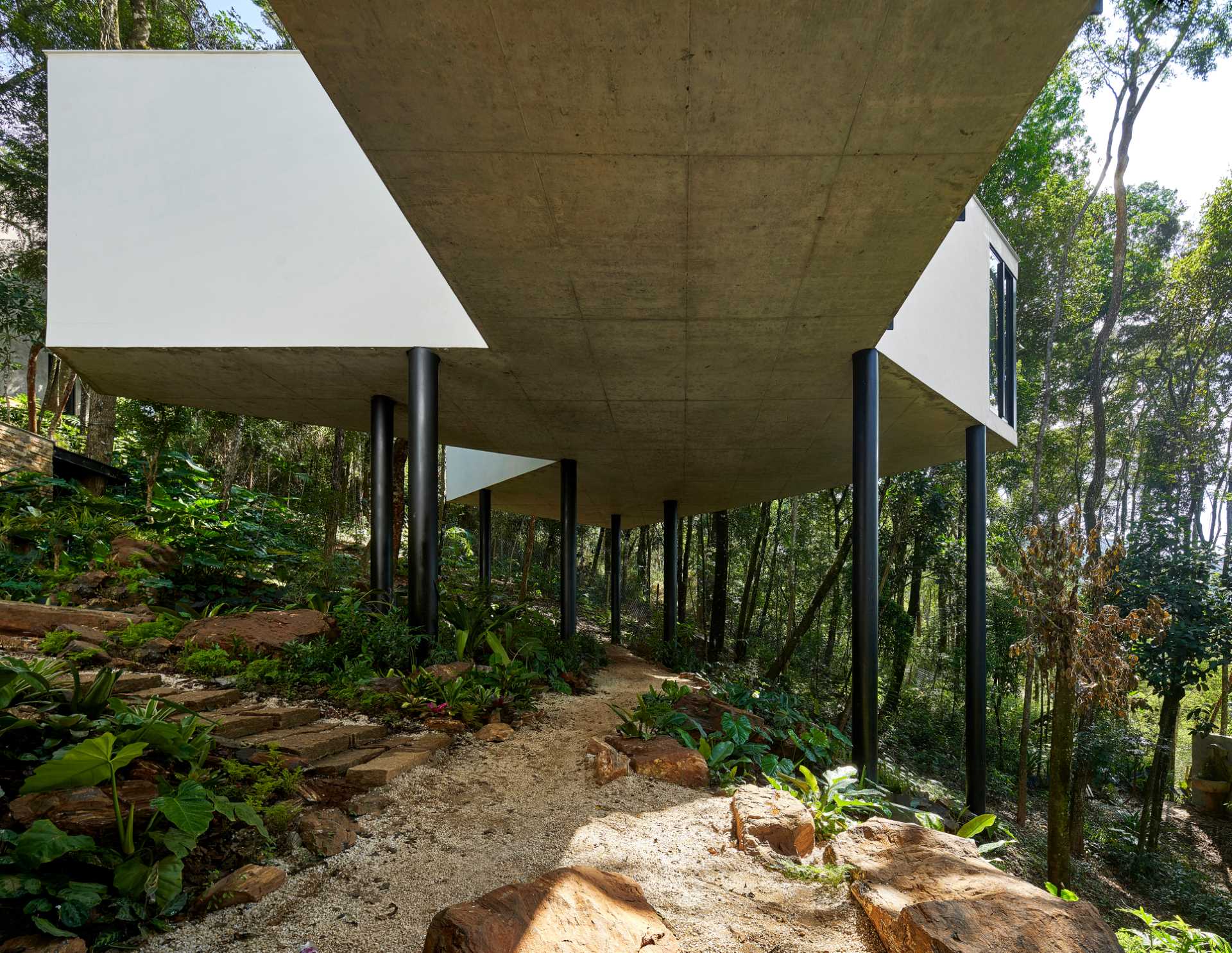 A modern house with a white exterior sits atop black stilts in the rainforest of Nova Lima, Brazil.