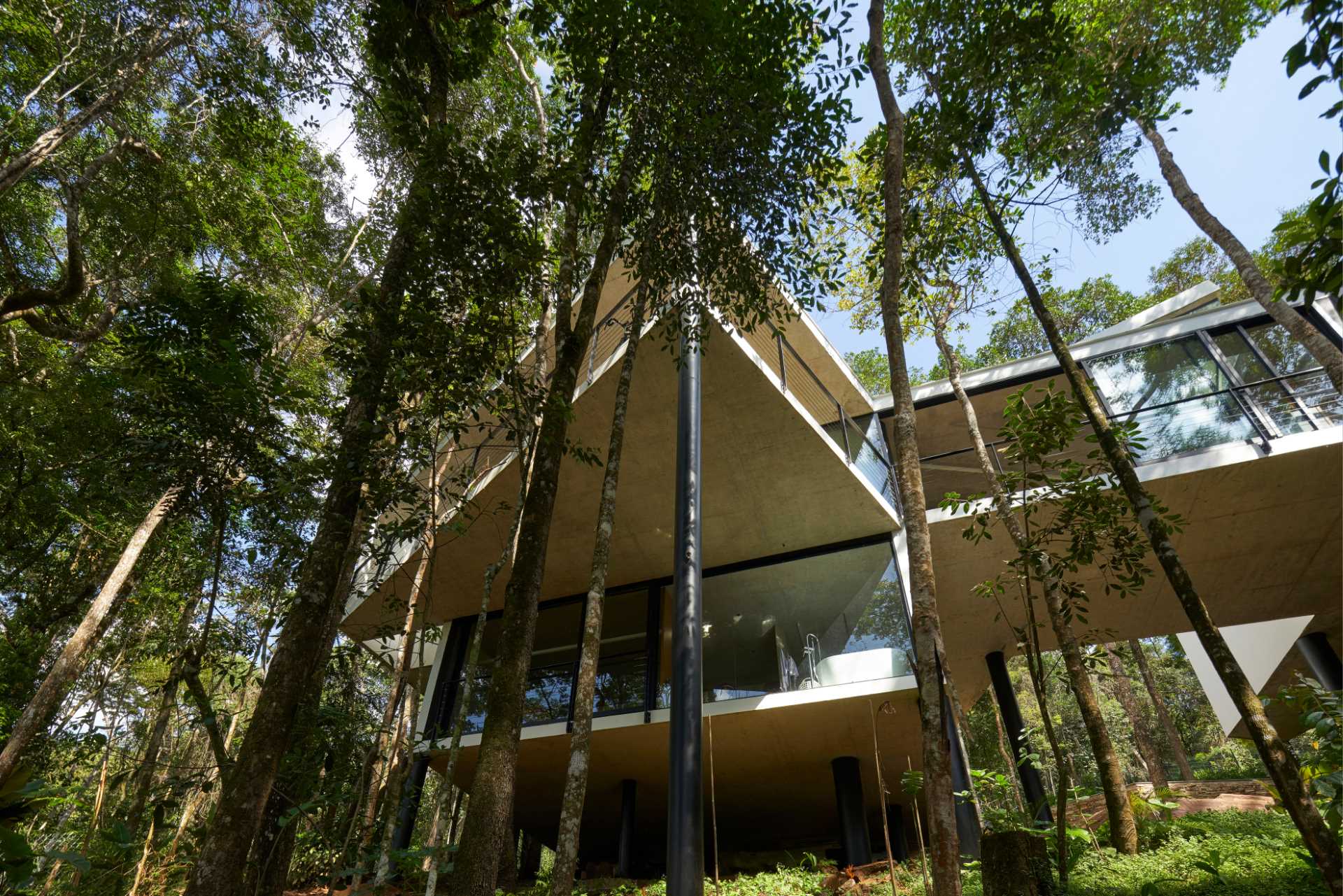 A modern house with a white exterior sits atop black stilts in the rainforest of Nova Lima, Brazil.