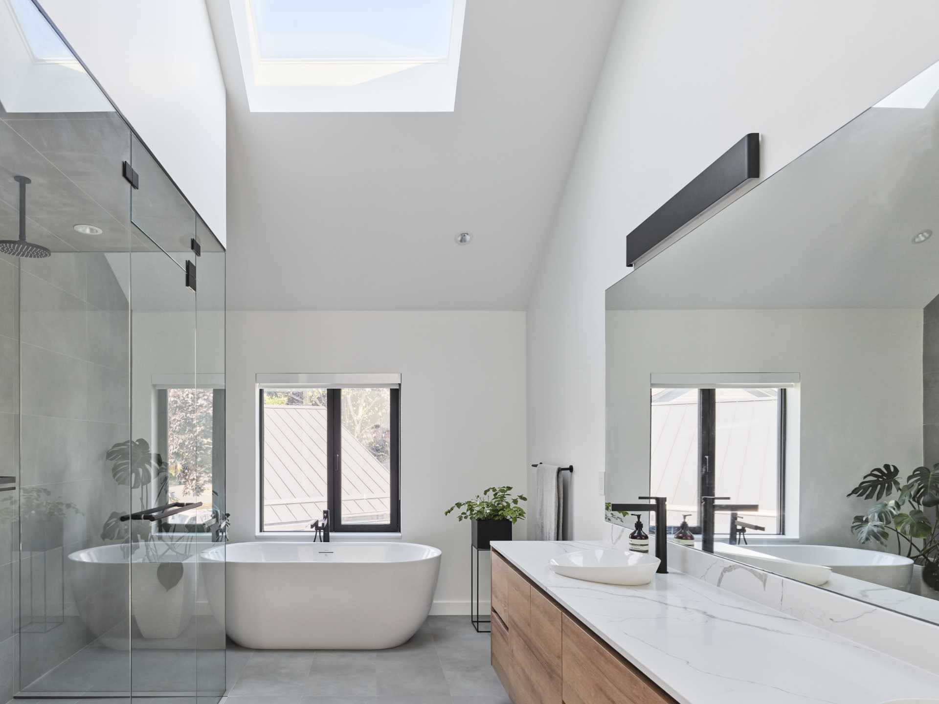 In this modern en-suite bathroom, there's a double vanity, a glass-enclosed walk-in shower, and a freestanding bathtub by the window.