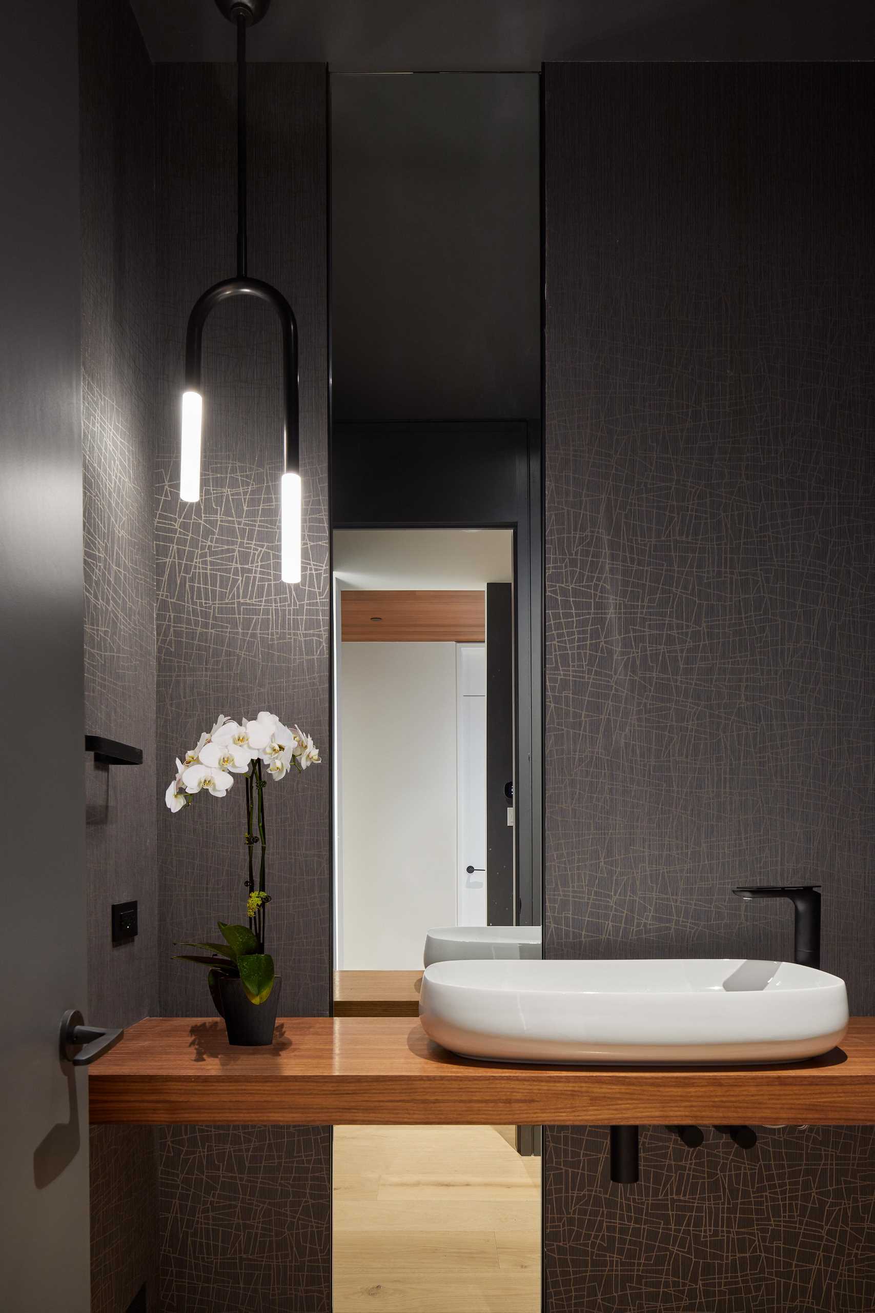 A powder room with dark graphic wallpaper and wood vanity.