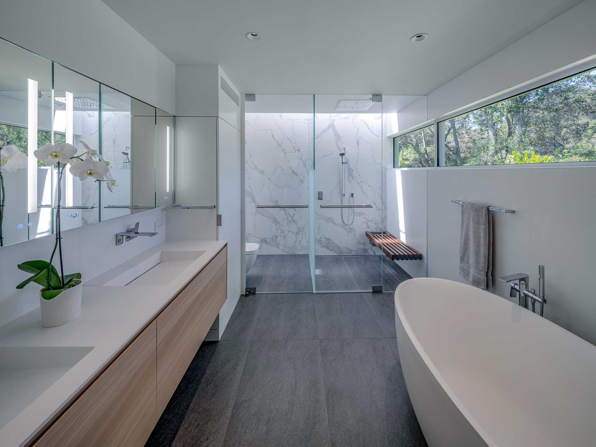 This modern en-suite bathroom includes a double vanity and a freestanding bathtub, as well as a glass-enclosed shower and toilet room.