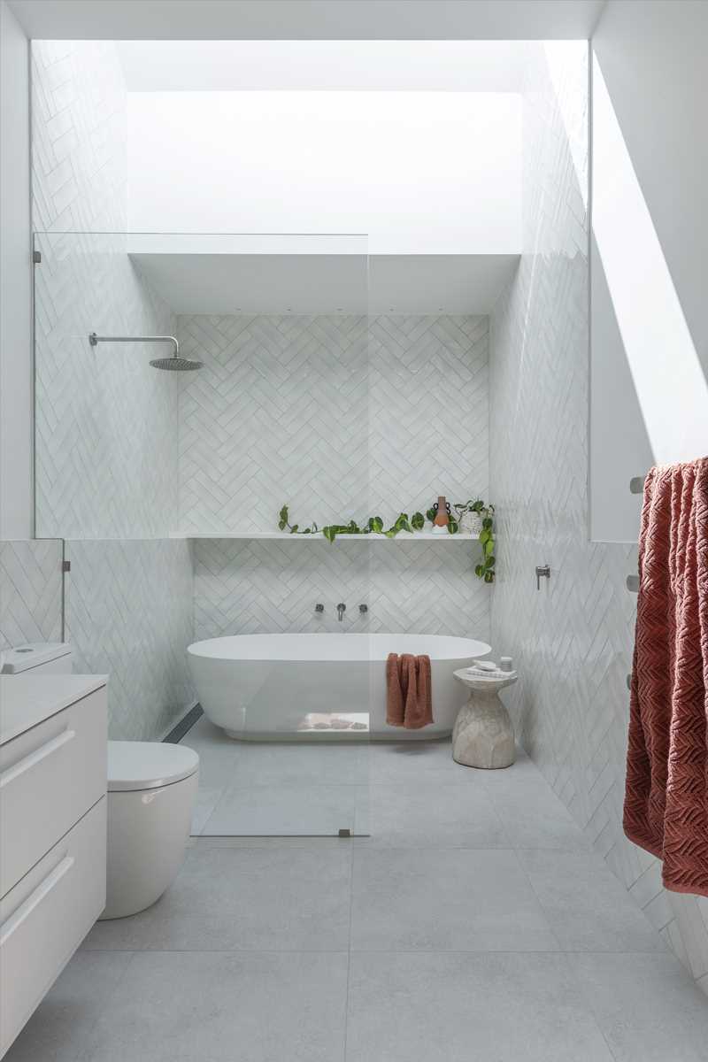 This primary bathroom is a calm retreat, with white tiles lining the walls, a skylight, and a freestanding bathtub. There's also a double vanity with an arched mirror.