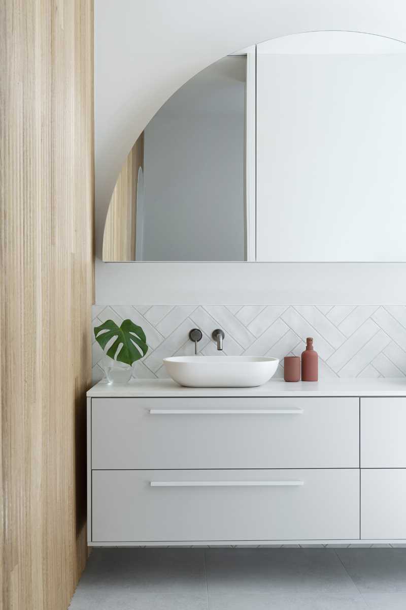 This primary bathroom is a calm retreat, with white tiles lining the walls, a skylight, and a freestanding bathtub. There's also a double vanity with an arched mirror.