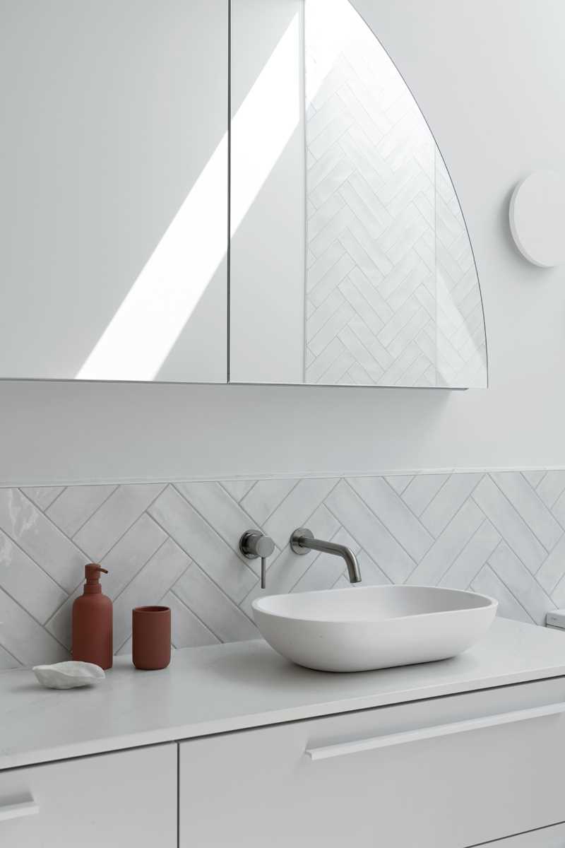 This primary bathroom is a calm retreat, with white tiles lining the walls, a skylight, and a freestanding bathtub. There's also a double vanity with an arched mirror.