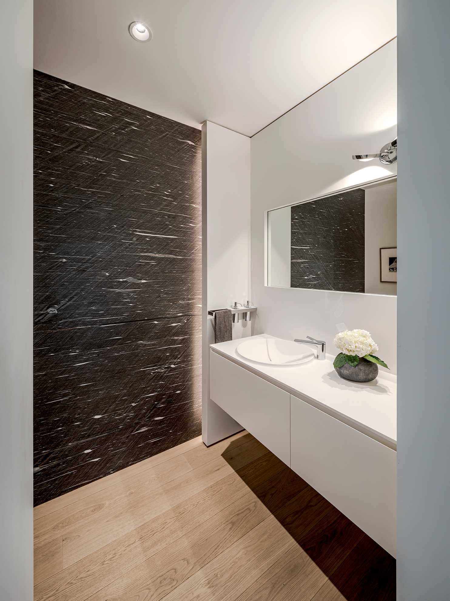 This modern bathroom has a dark accent wall with hidden lighting that contrasts the white vanity and walls.