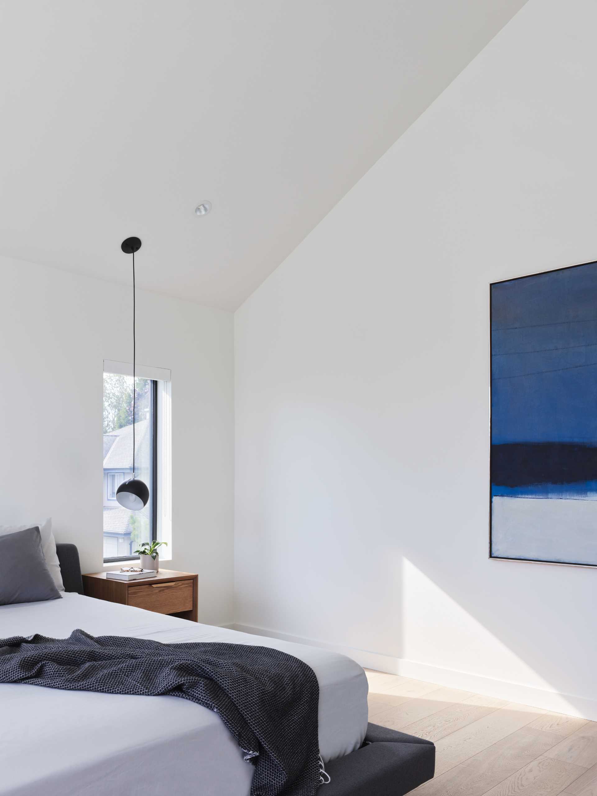 In this modern bedroom, blue artwork adds a pop of color, while a pendant light acts as a bedside lamp.