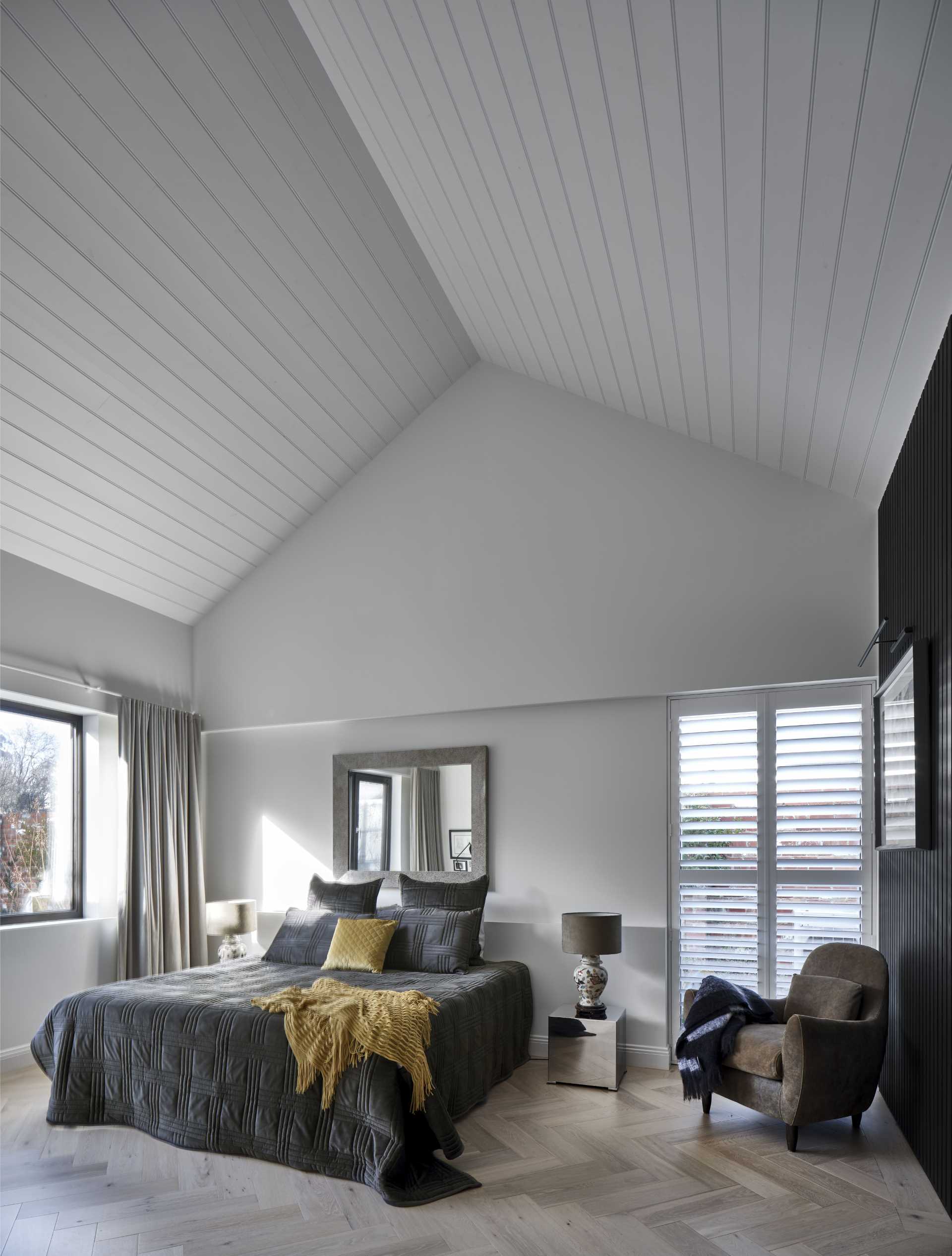 In this contemporary bedroom, a high ceiling makes the room feel larger, while black elements tie back into the black accents in the kitchen and living room.