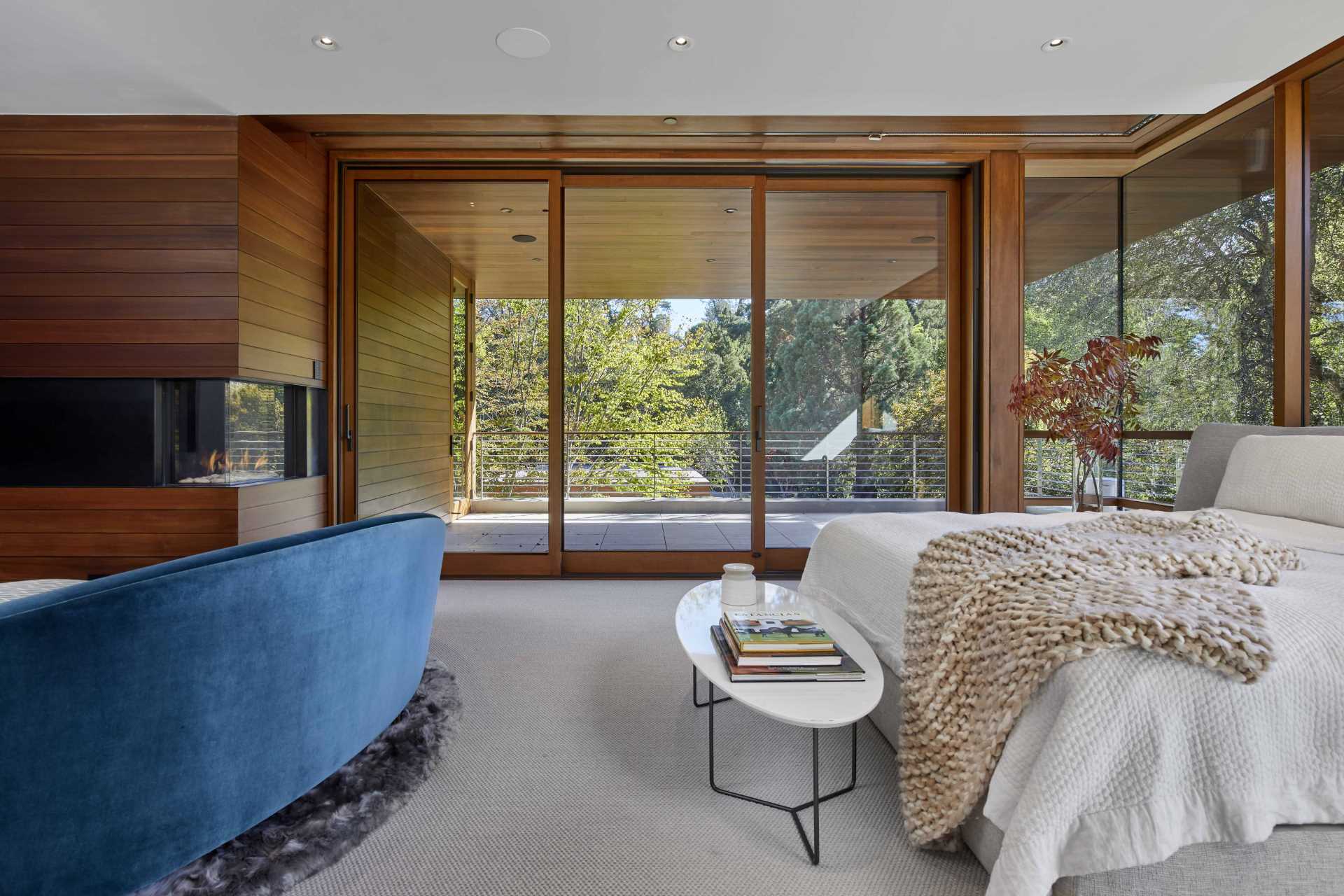 In this primary bedroom, glass walls provide a view of the trees, and a sliding glass door opens to a private balcony.