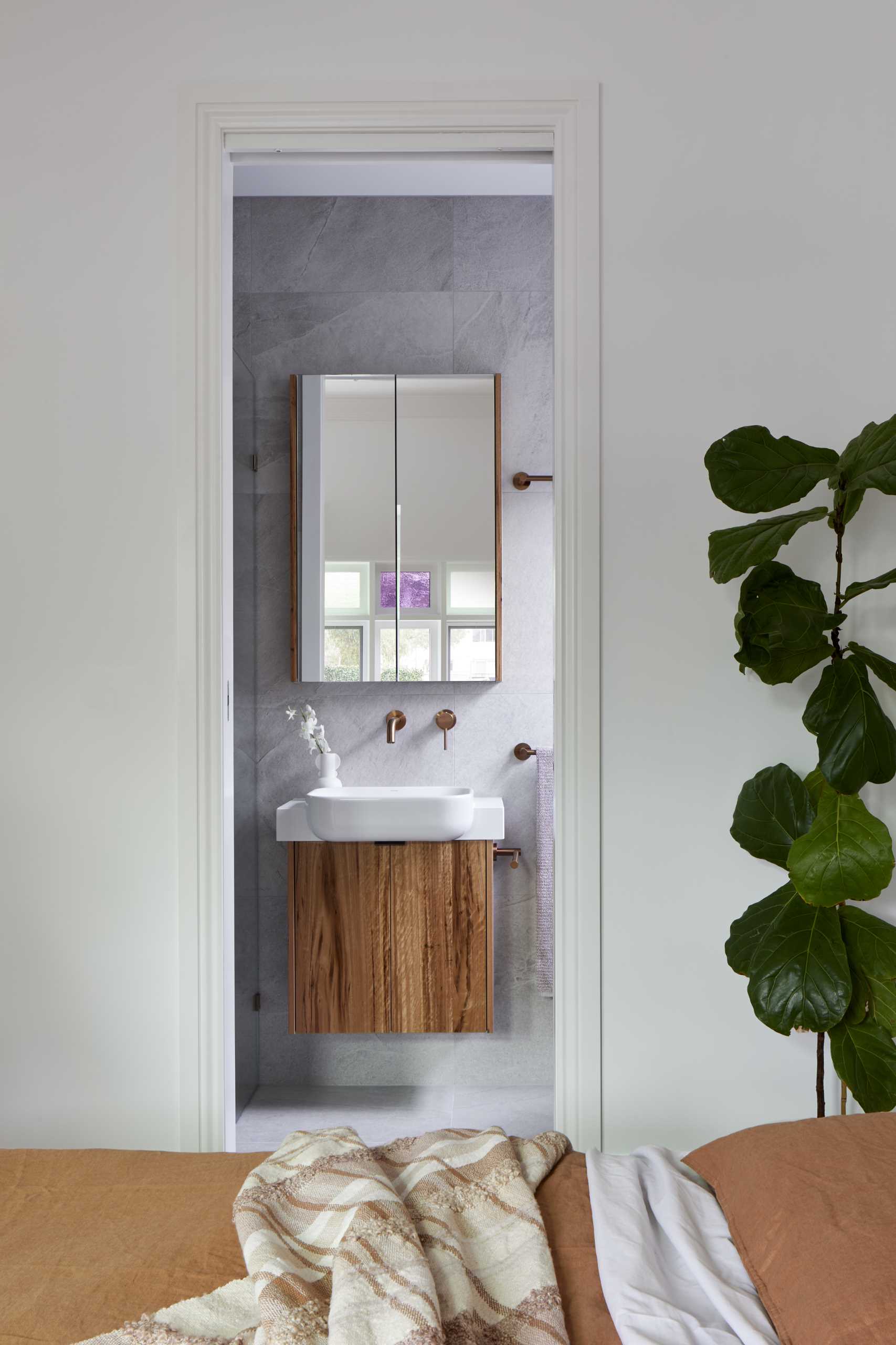 This modern en-suite bathroom has a single vanity with a glass-enclosed walk-in shower on one side and a freestanding bathtub with a shelving niche on the other.