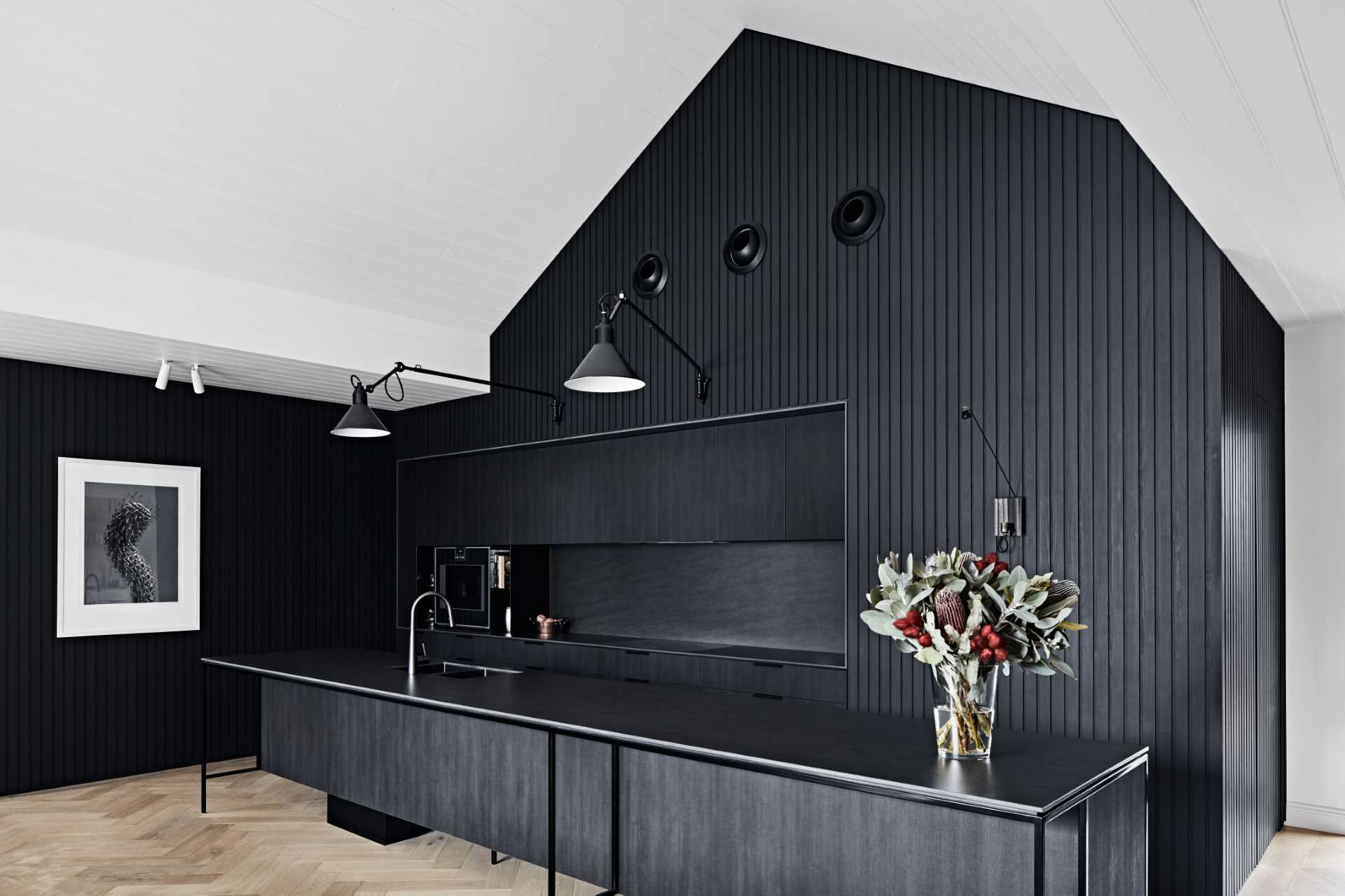 The striking black kitchen facilitates the owners’ love for cooking and entertaining and includes hardware-free cabinets, black appliances, black countertops, and a matching long island with black kitchen faucet and sink.