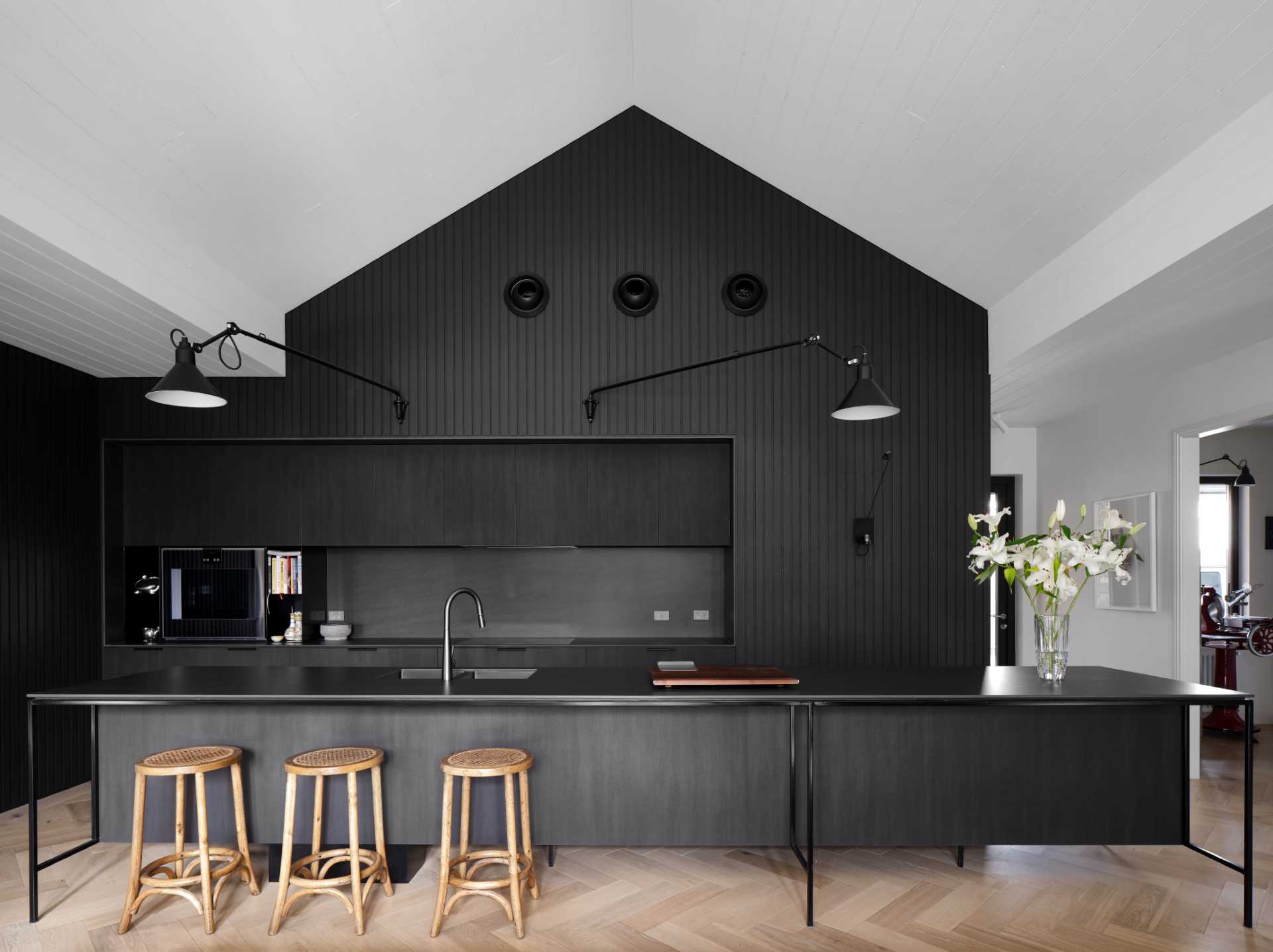 The striking black kitchen facilitates the owners’ love for cooking and entertaining and includes hardware-free cabinets, black appliances, black countertops, and a matching long island with black kitchen faucet and sink.