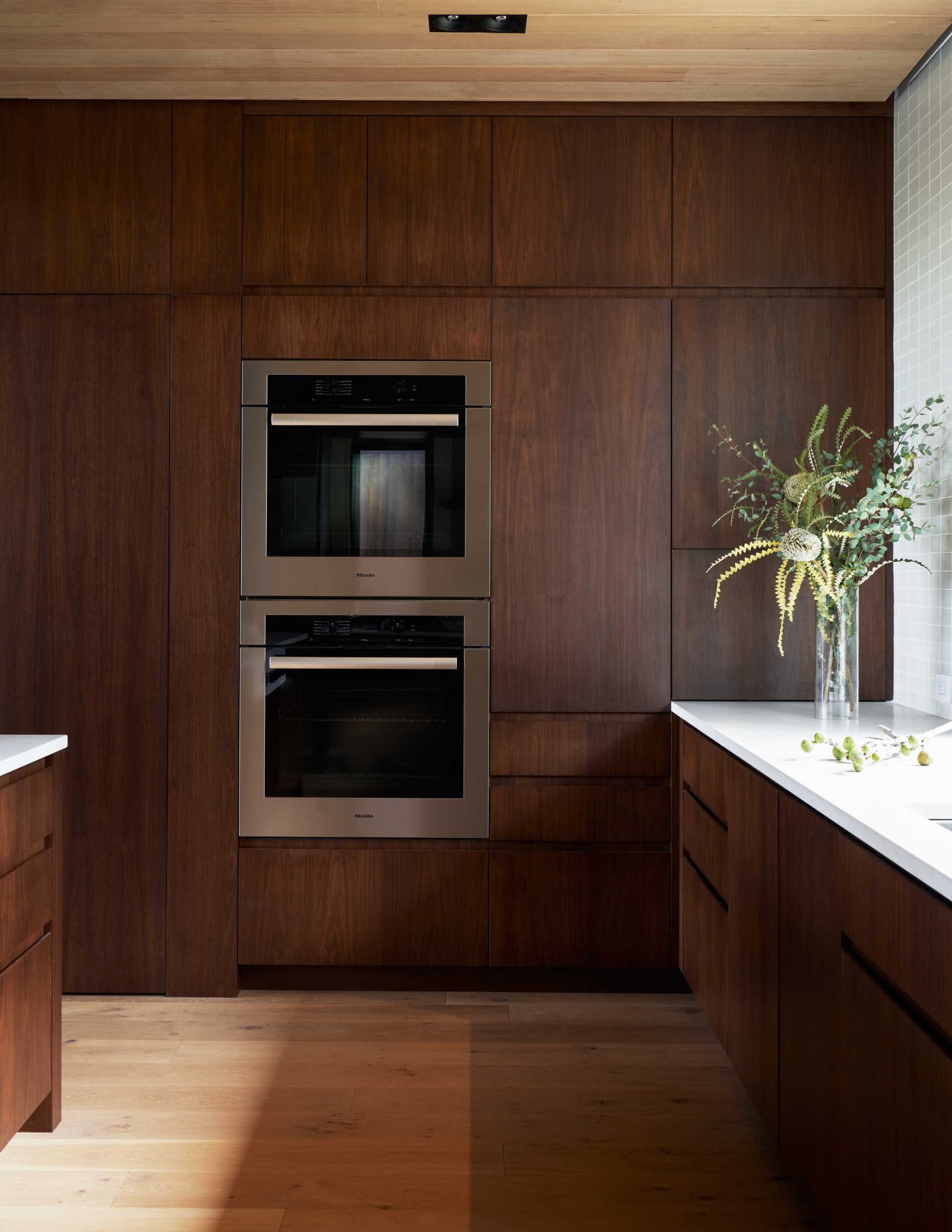 A modern kitchen with dark walnut cabinets and white countertops.