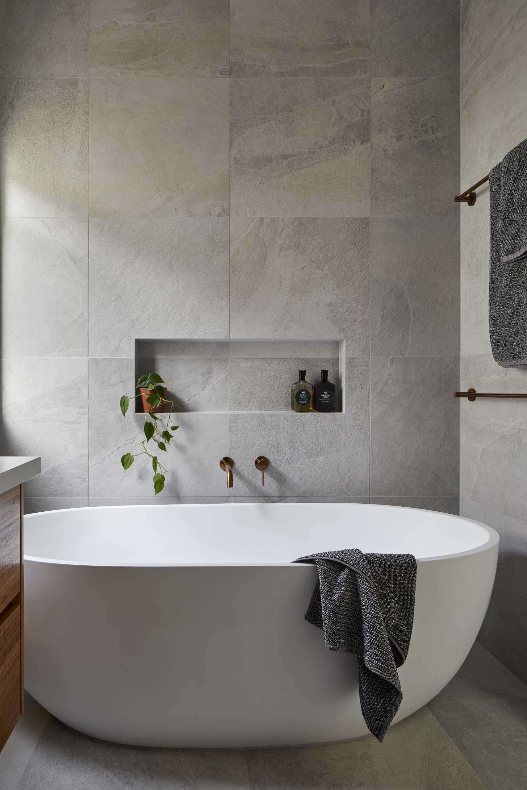 This modern en-suite bathroom has a single vanity with a glass-enclosed walk-in shower on one side and a freestanding bathtub with a shelving niche on the other.