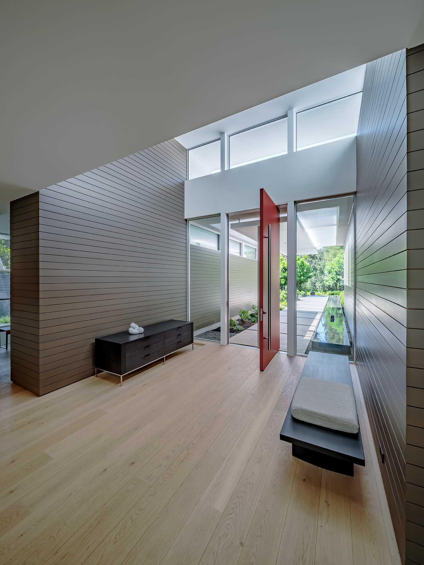 The pivoting red front door opens to the entryway that's been minimally furnished with a bench and low console.