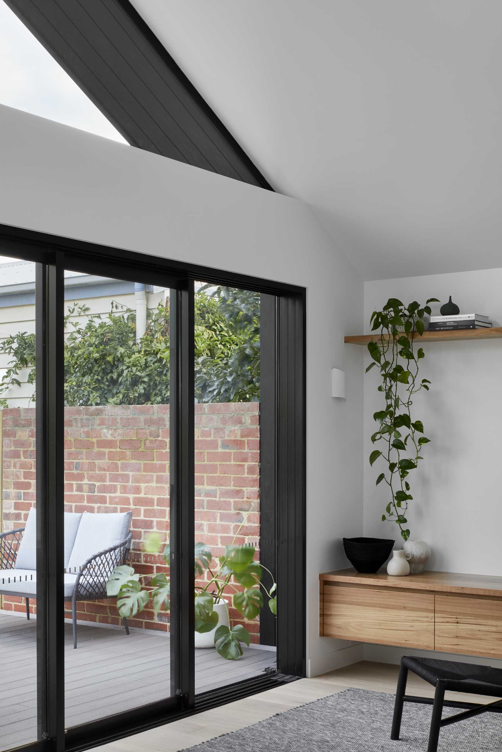 Sliding doors connect the living room and the deck, creating an indoor/outdoor living environment. A floating wood cabinet and shelves line the wall, while a black fireplace adds warmth to the interior.