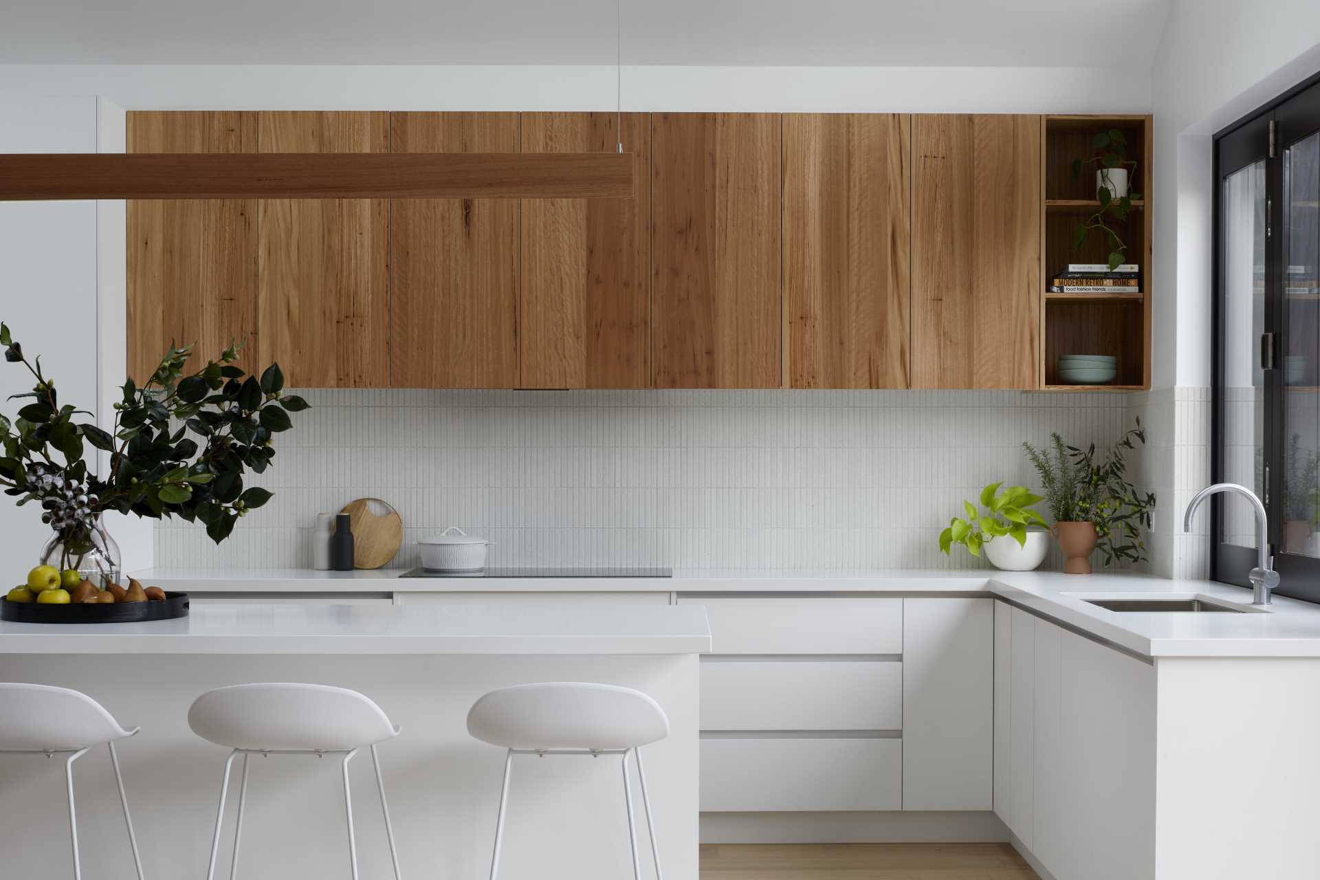 The folding pass-through window connects the kitchen to the outdoor space, while the rest of the kitchen includes white and wood cabinets, a skylight, and an island with open shelving.