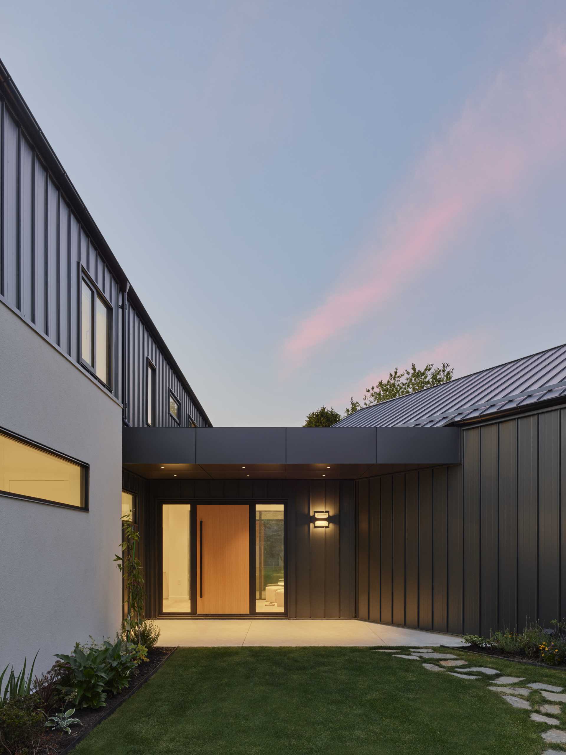 The front door of this modern home opens to the glass hallway, with windows providing a glimpse of the yard.