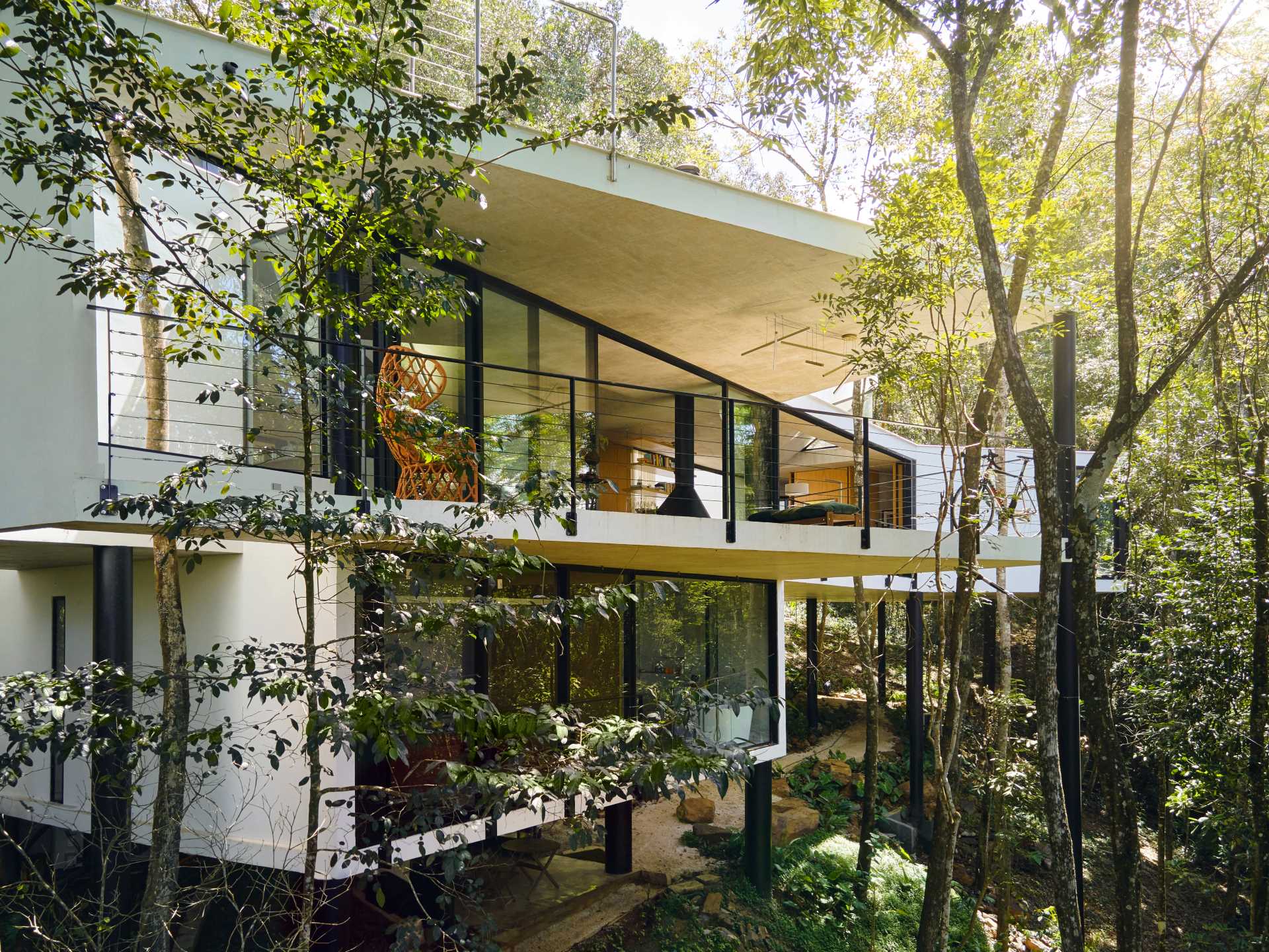 A modern house with a white exterior sits atop black stilts in the rainforest of Nova Lima, Brazil.