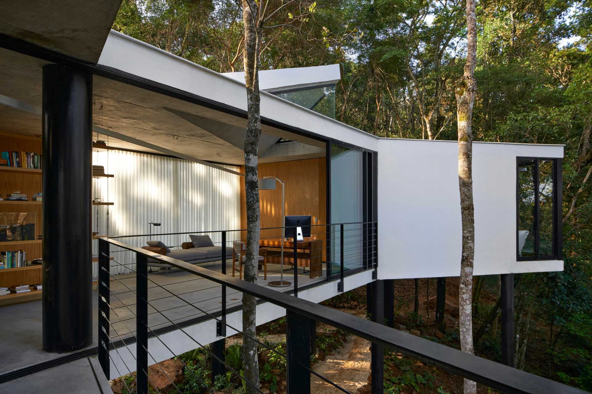 A modern house with a white exterior sits atop black stilts in the rainforest of Nova Lima, Brazil.