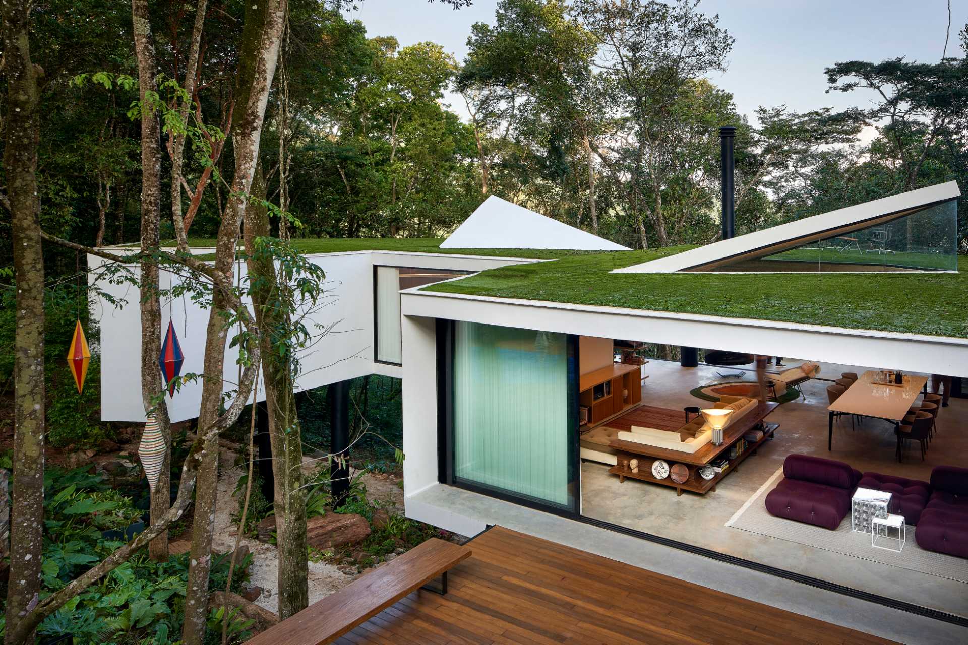 A modern house with a white exterior sits atop black stilts in the rainforest of Nova Lima, Brazil.