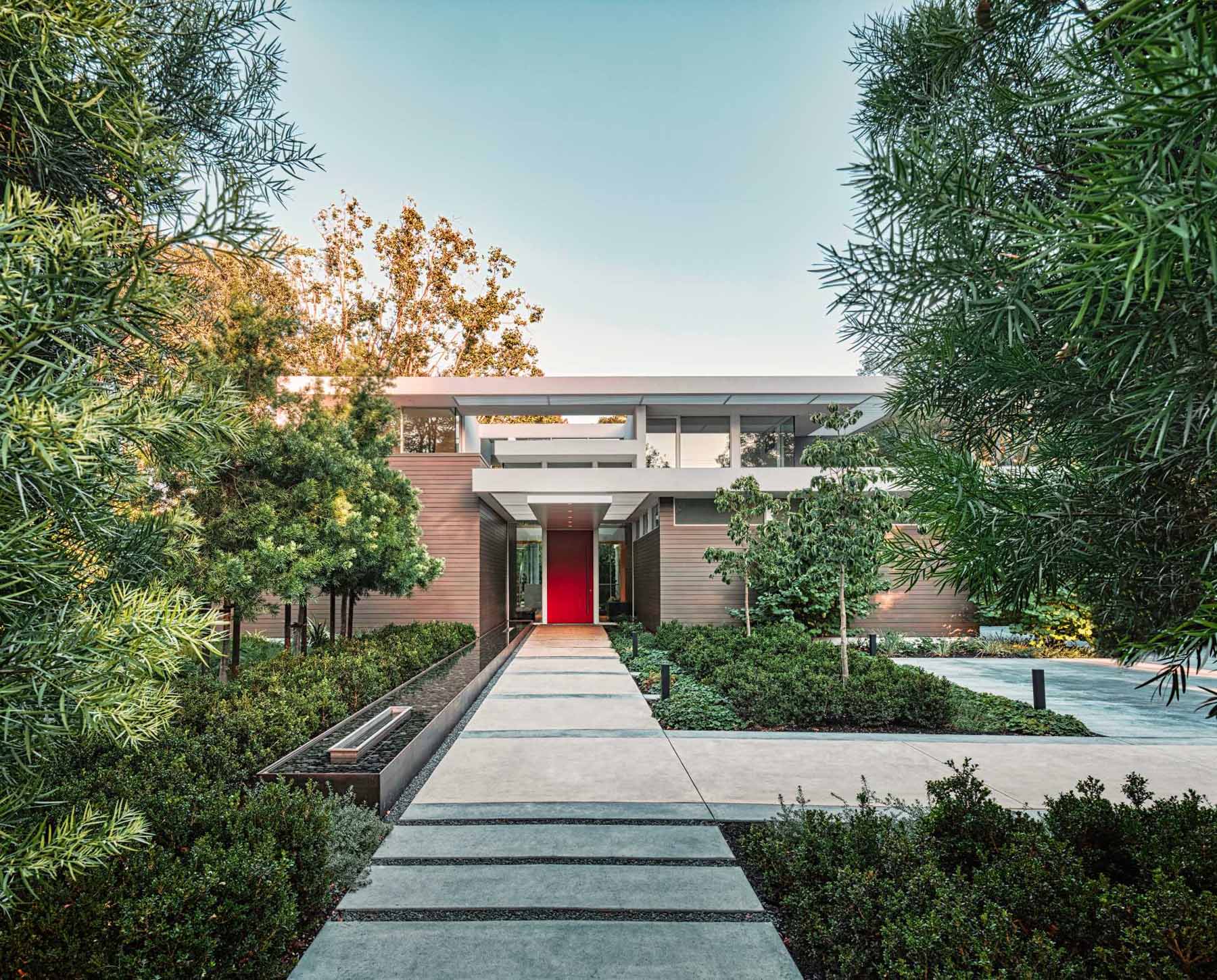 At the front of this modern home, a path guides visitors through the garden and to the pivoting red front door and entryway.