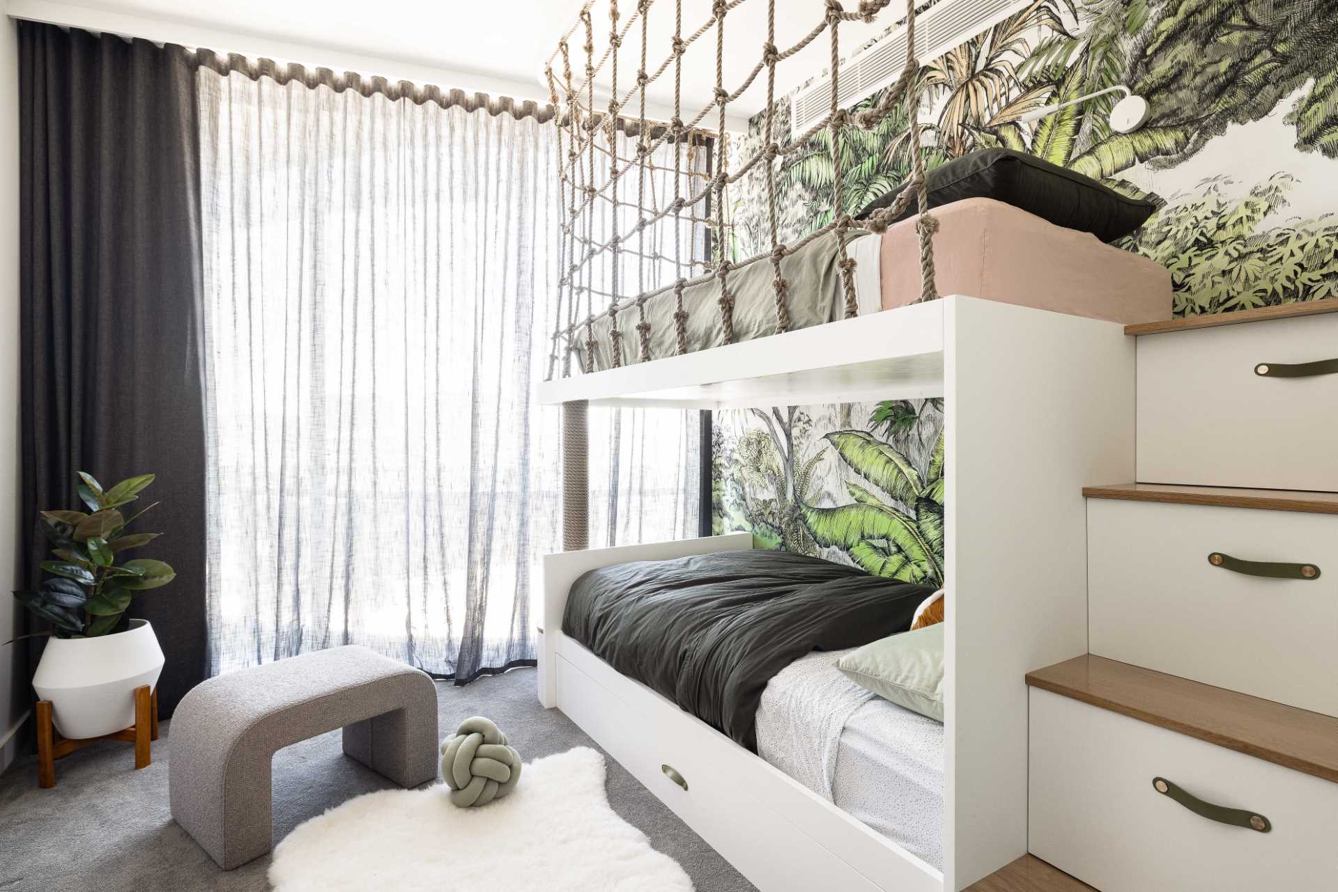 A modern jungle-themed bedroom for two brothers includes bunk beds, rope work, stairs with storage, and tree-top wallpaper.