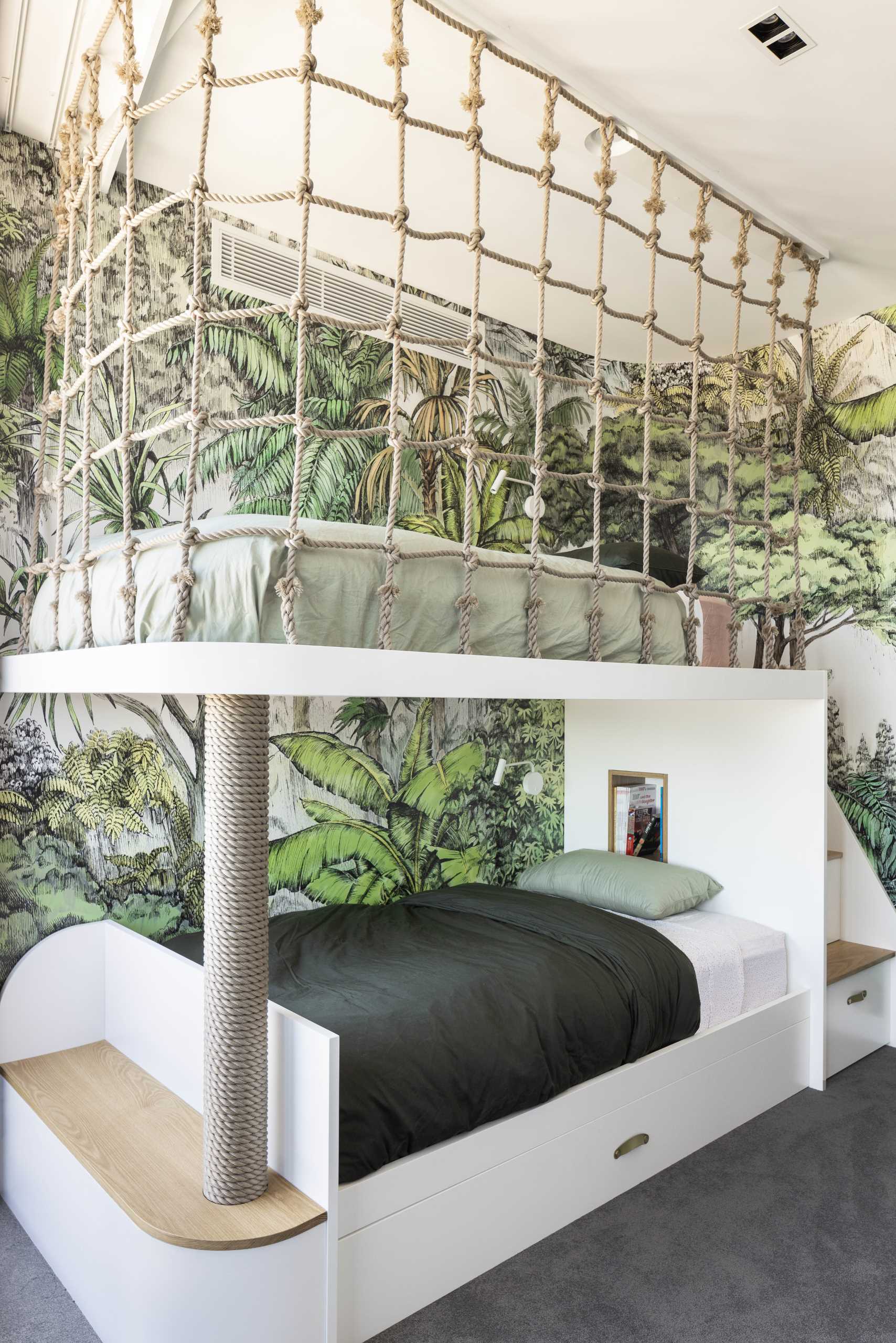 A modern jungle-themed bedroom for two brothers includes bunk beds, rope work, stairs with storage, and tree-top wallpaper.