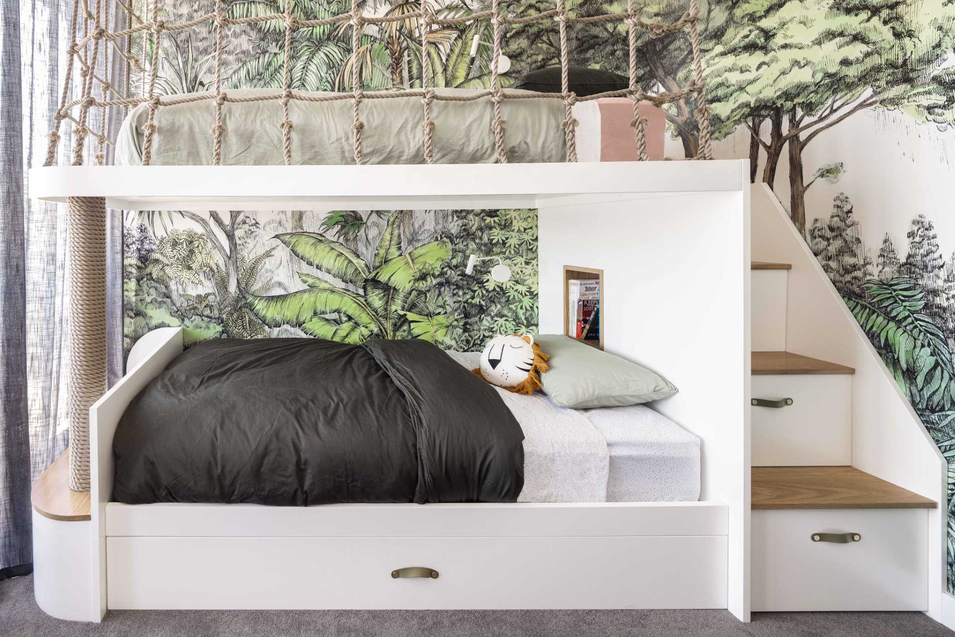 A modern jungle-themed bedroom for two brothers includes bunk beds, rope work, stairs with storage, and tree-top wallpaper.