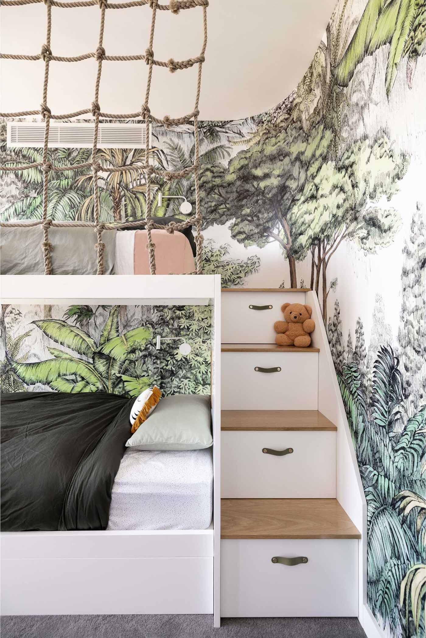 A modern jungle-themed bedroom for two brothers includes bunk beds, rope work, stairs with storage, and tree-top wallpaper.