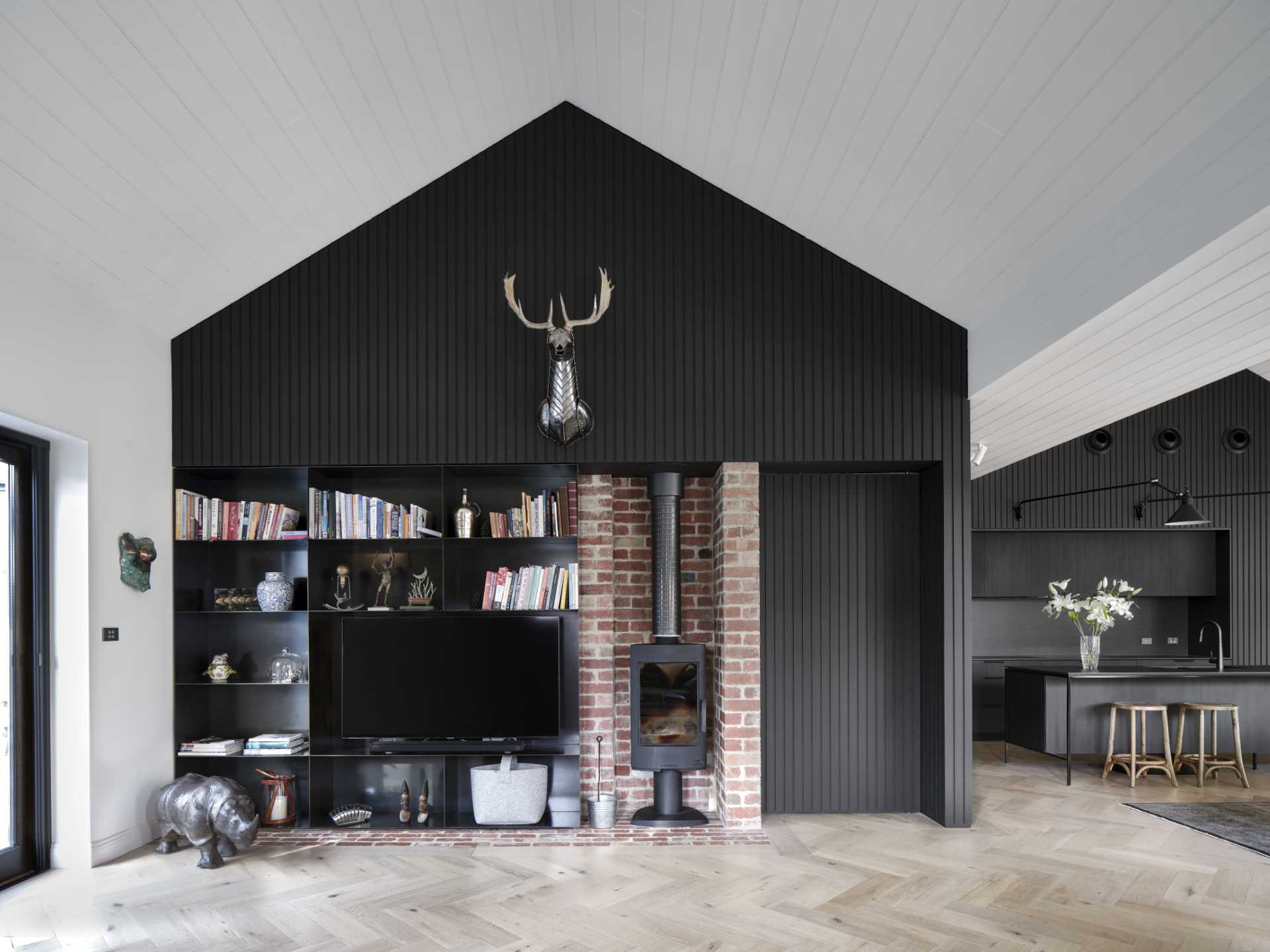 The black design of the kitchen is also utilized in the living room, with an accent wall that includes black metal shelving and a fireplace.