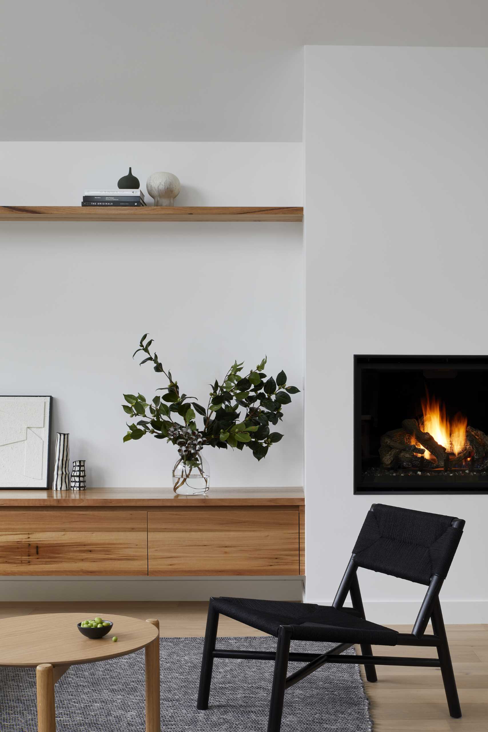 Sliding doors connect the living room and the deck, creating an indoor/outdoor living environment. A floating wood cabinet and shelves line the wall, while a black fireplace adds warmth to the interior.