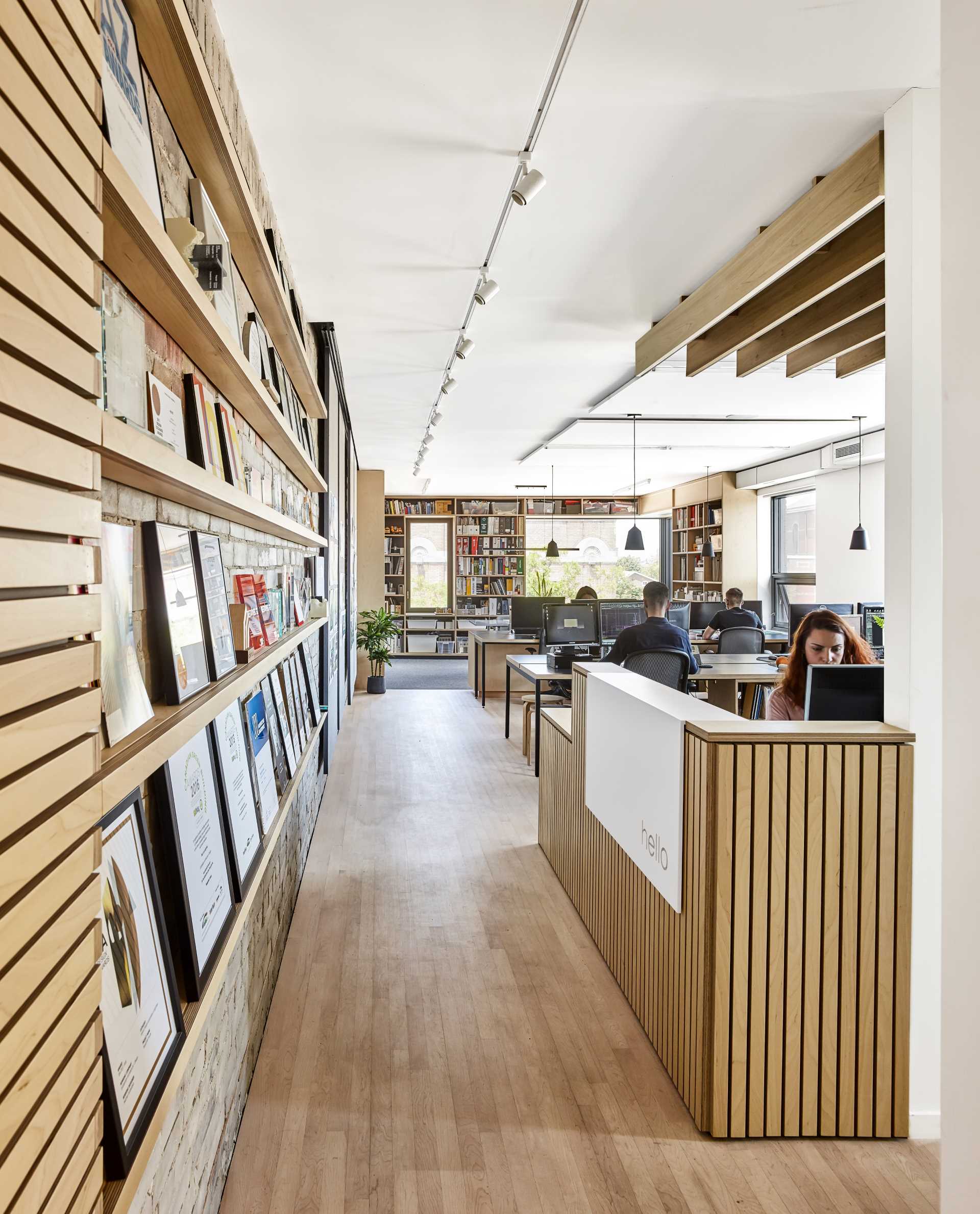 A modern office with wood slats and a white Corian waterfall panel that greets visitors with an inscribed “hello” at the reception desk.