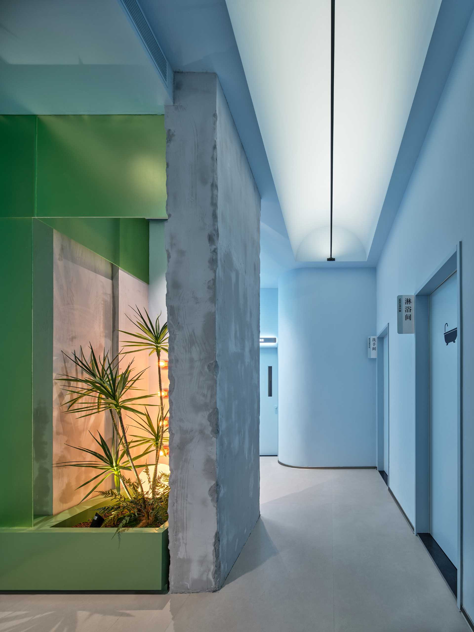 The hallway includes a small planter and original concrete wall, while the light blue hallway leads to the various treatment rooms of this modern skincare center.