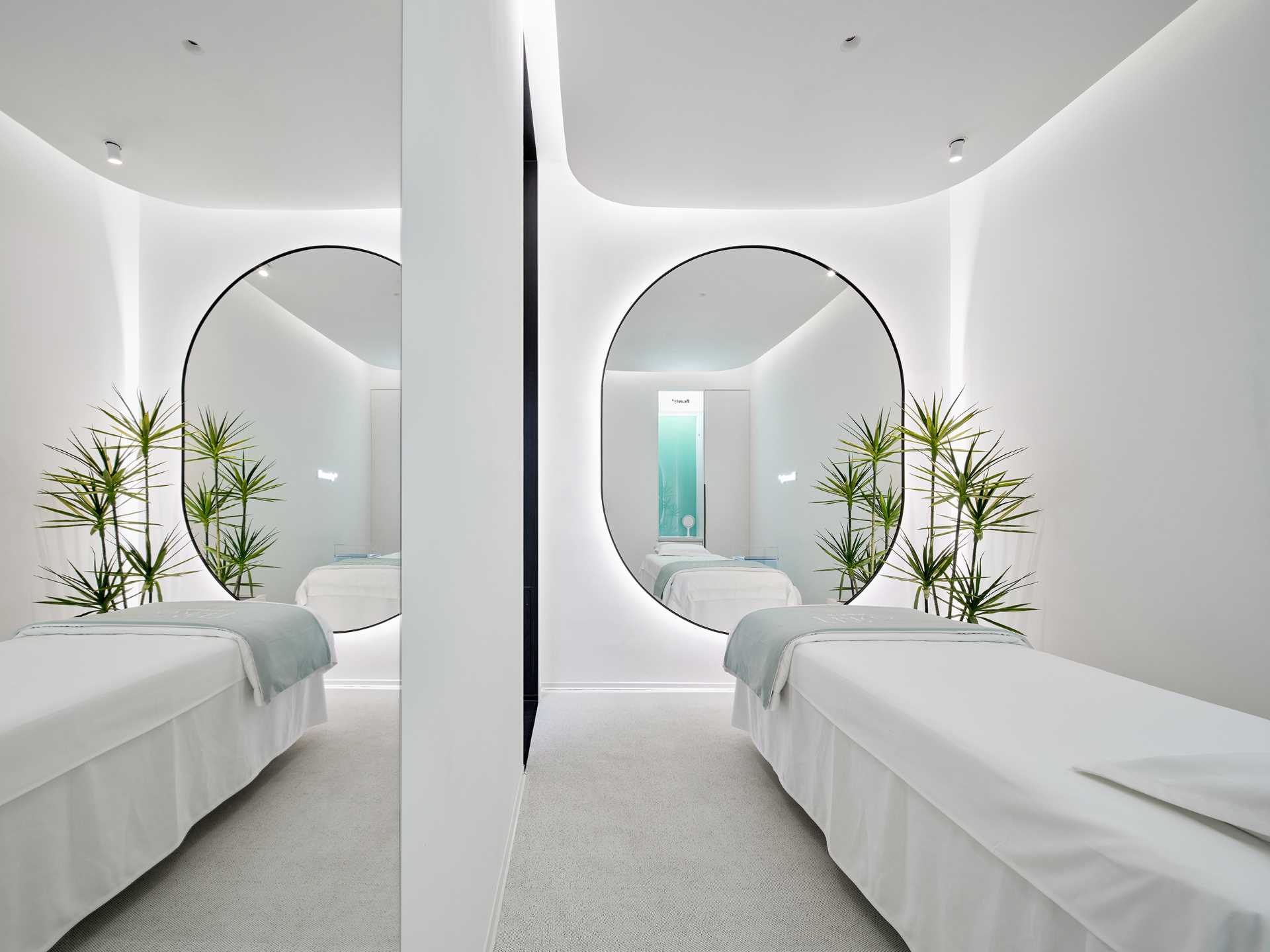 The single-person treatment room has a rectangular layout with a rounded ceiling detail to soften the corners. A large mirror makes the space feel larger, while the opposite wall features a blue-green gradient glass accent.